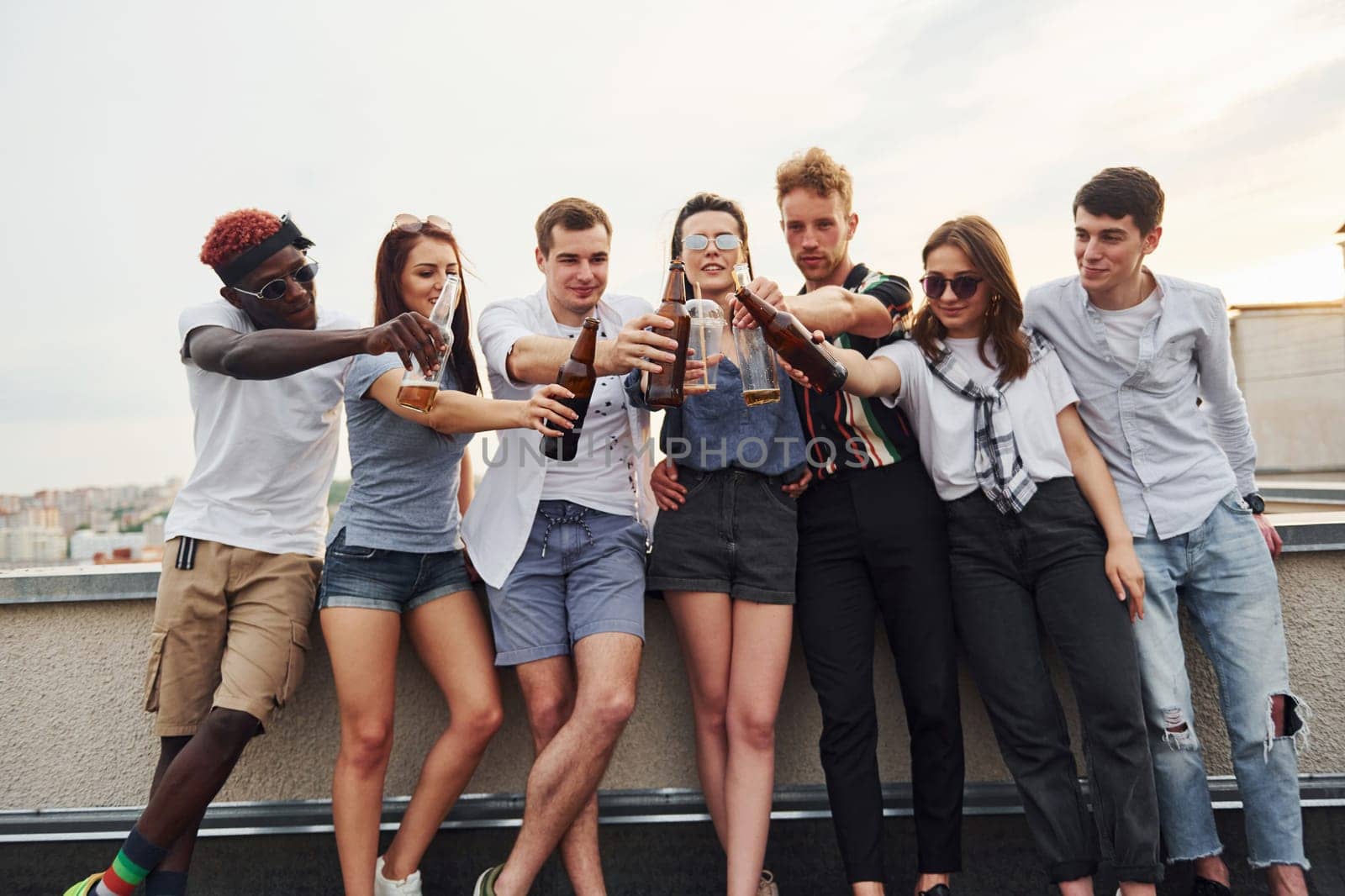 Standing with alcohol at the edge of rooftop. Group of young people in casual clothes have a party together at daytime.