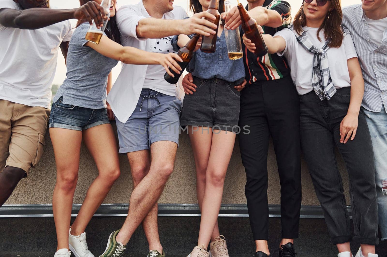 Standing with alcohol at the edge of rooftop. Group of young people in casual clothes have a party together at daytime.