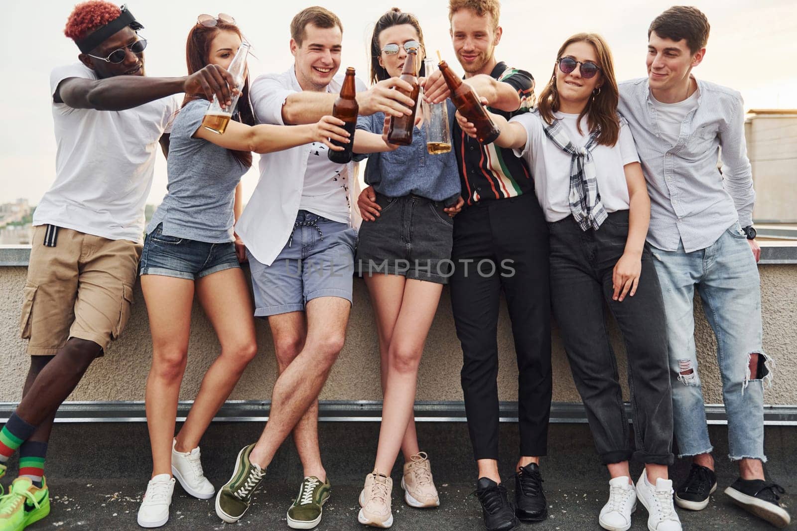 Standing with alcohol at the edge of rooftop. Group of young people in casual clothes have a party together at daytime.