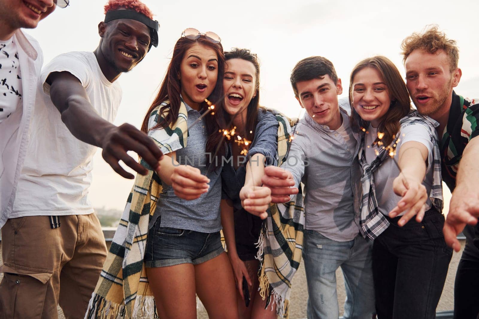 With sparklers in hands. Group of young people in casual clothes have a party at rooftop together at daytime.