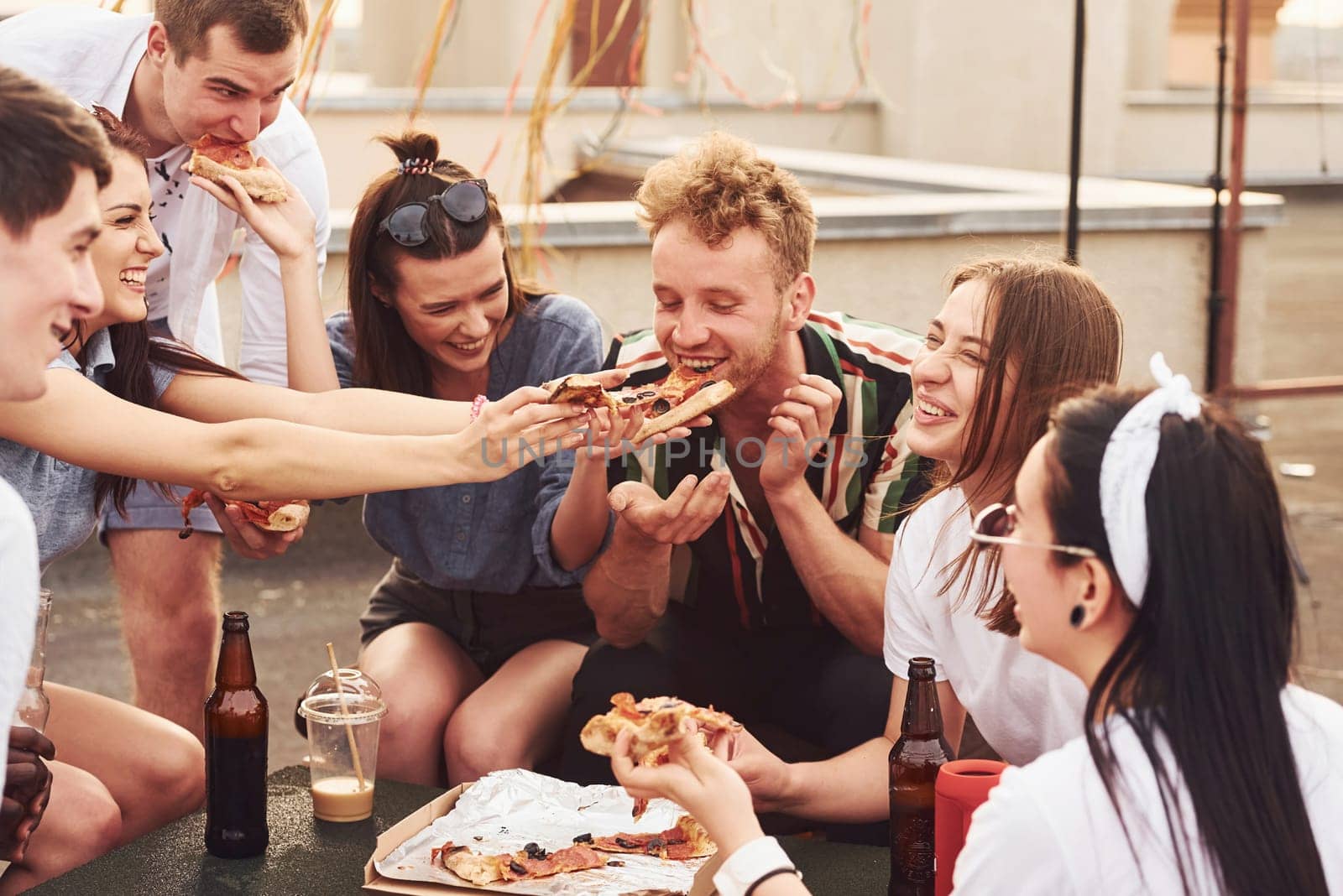 Delicious pizza. Group of young people in casual clothes have a party at rooftop together at daytime.