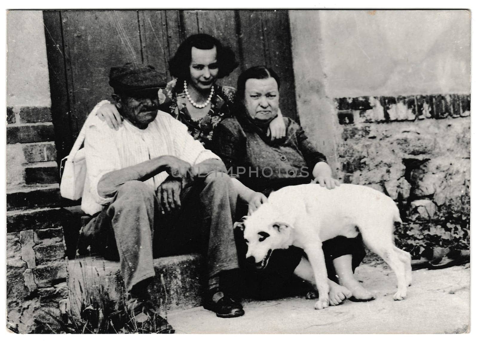 Retro photo shows rural people sit on a doorstep with dog. Black and white vintage photography by roman_nerud