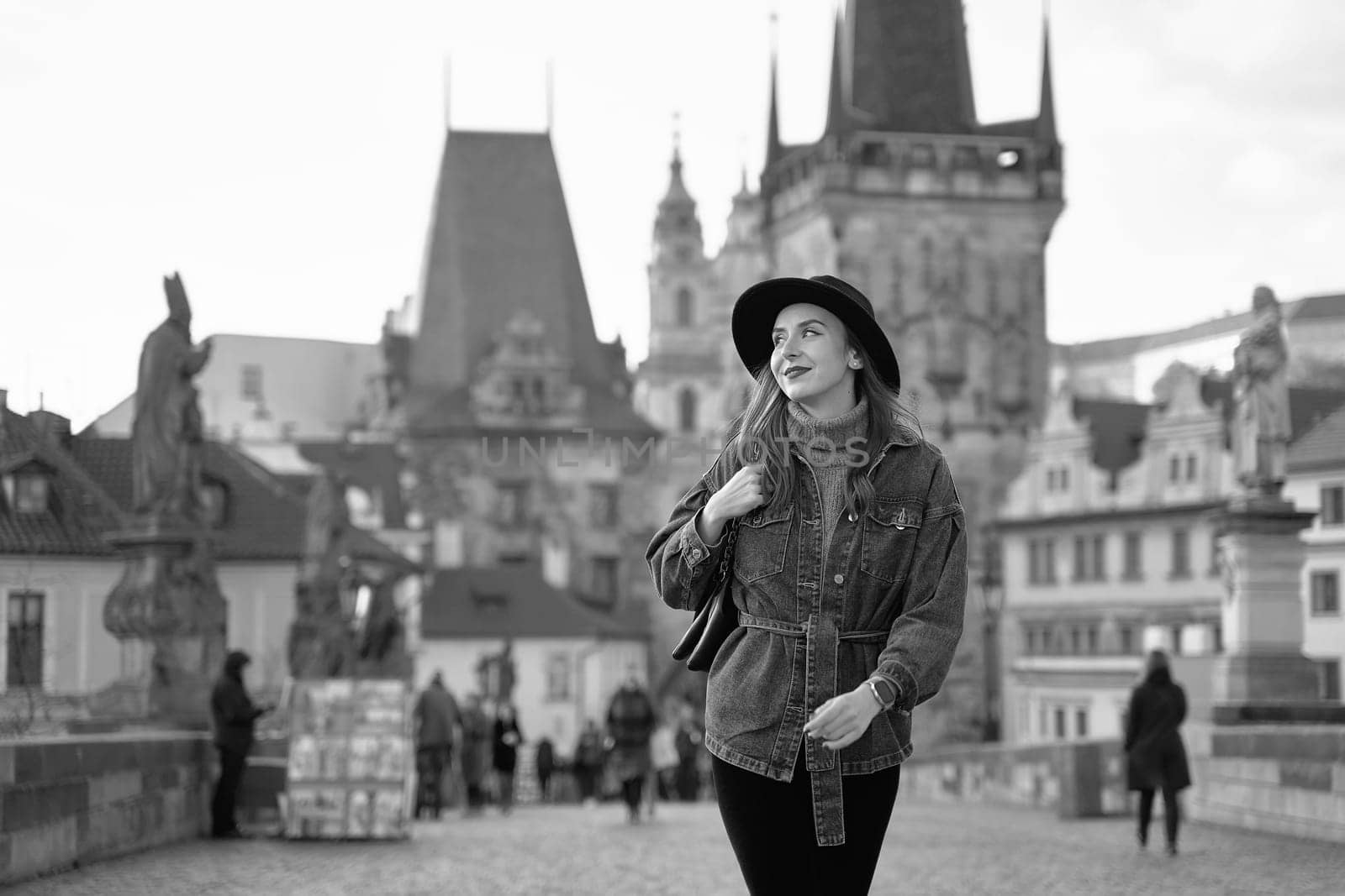 Female traveller tourist on the Charles Bridge in Prague, Czezh Repubic. Stylish beautiful young woman earing black hat. Elegant retro black and white portrait. by berezko