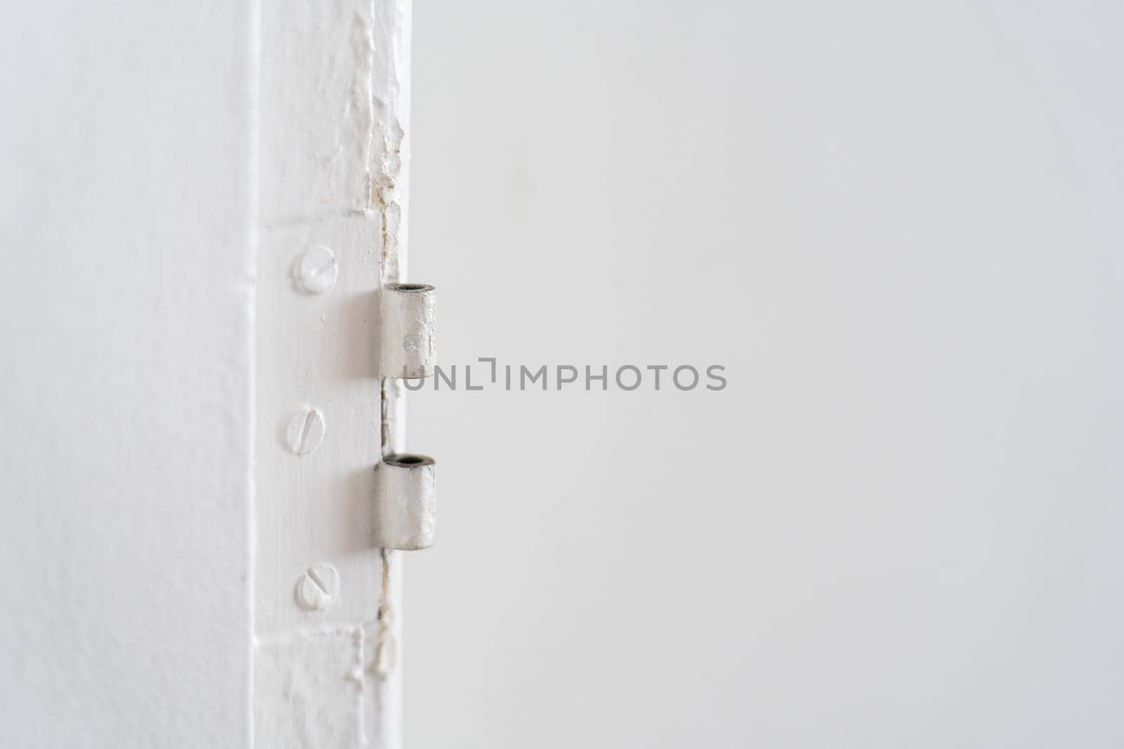 Detailed view of an antique hinge without a door, showing its rusty steel surface and hidden screws painted over on a white wall.