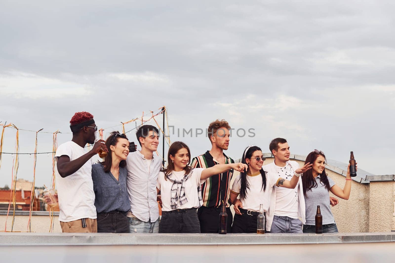 Group of young people in casual clothes have a party at rooftop together at daytime.