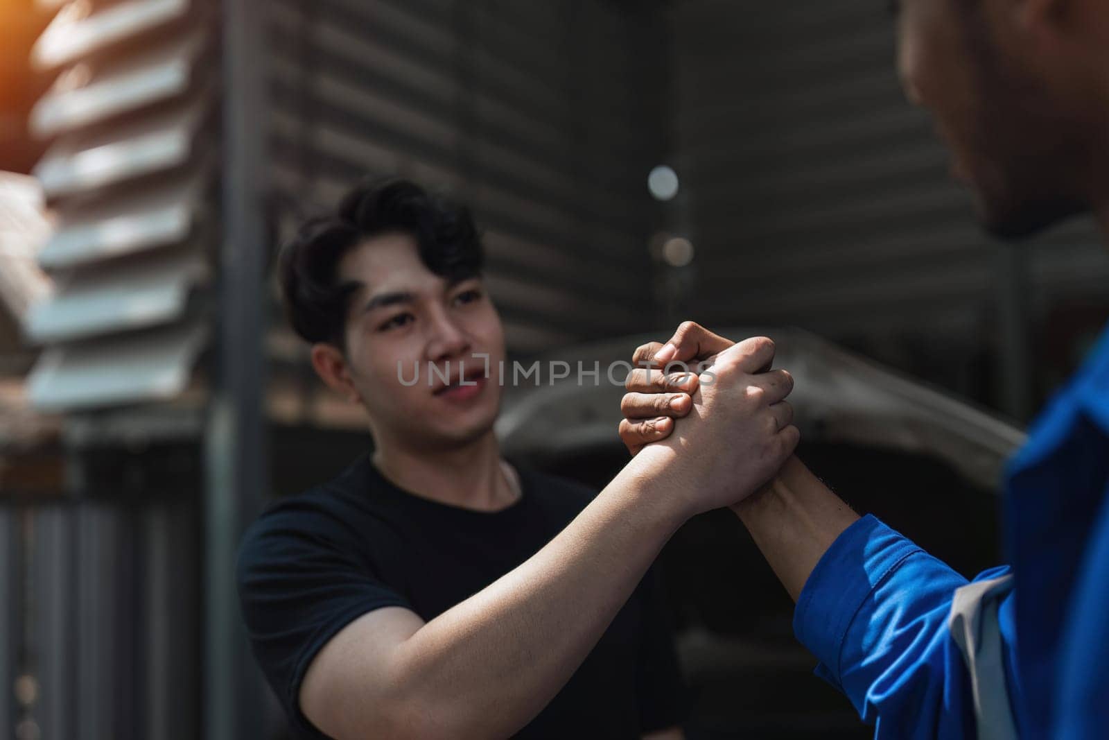 Young man client shaking hands with auto mechanic in red uniform having a deal at the car service.