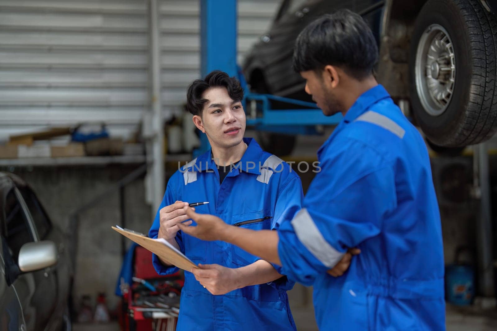 Mechanic man shows report to the asian coworker at garage, A man mechanic and his son discussing repairs done vehicle. Changing automobile business. by nateemee