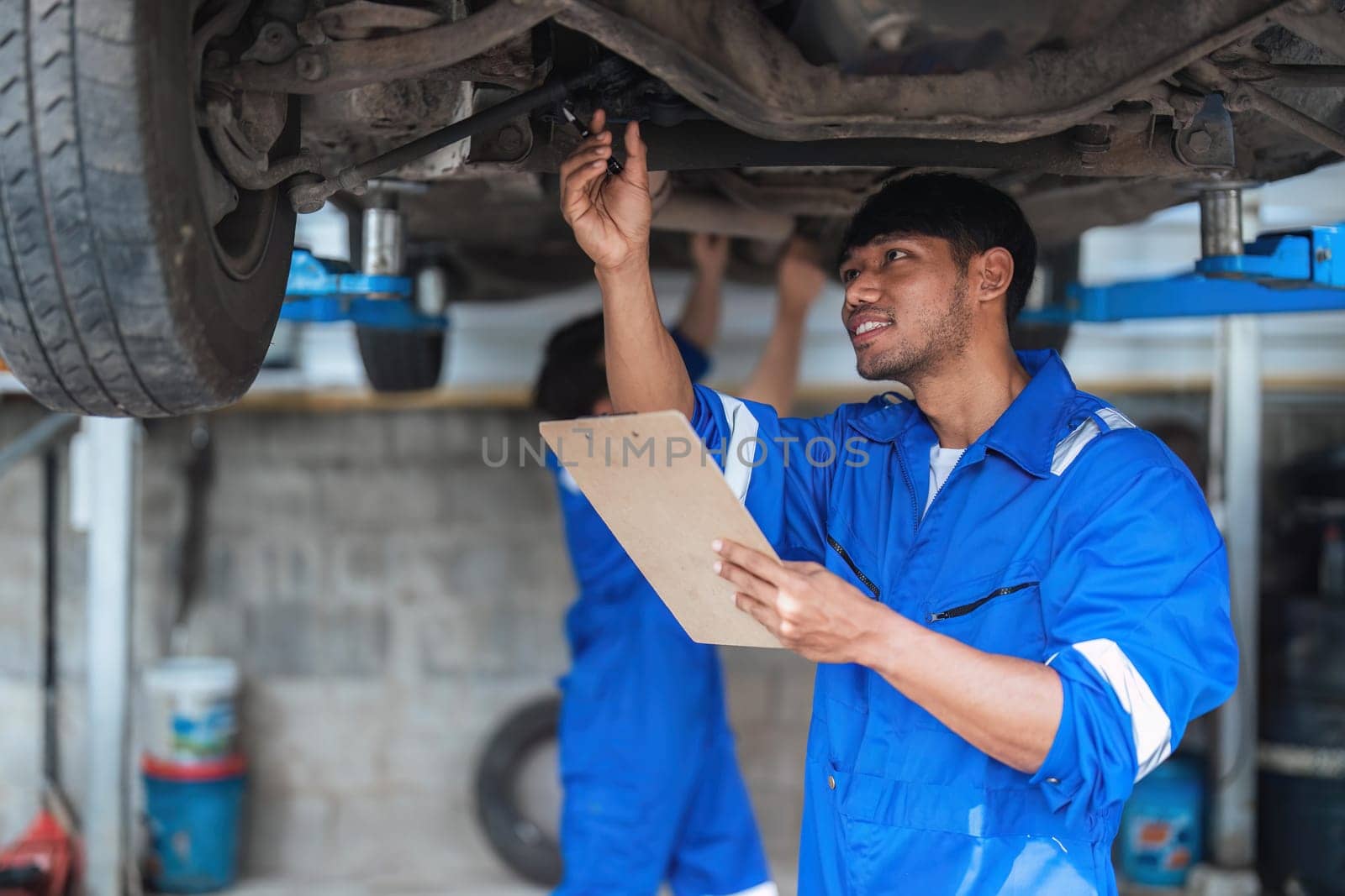 Vehicle service maintenance asian man checking under car condition in garage. Automotive mechanic maintenance checklist document. Car repair service concept.