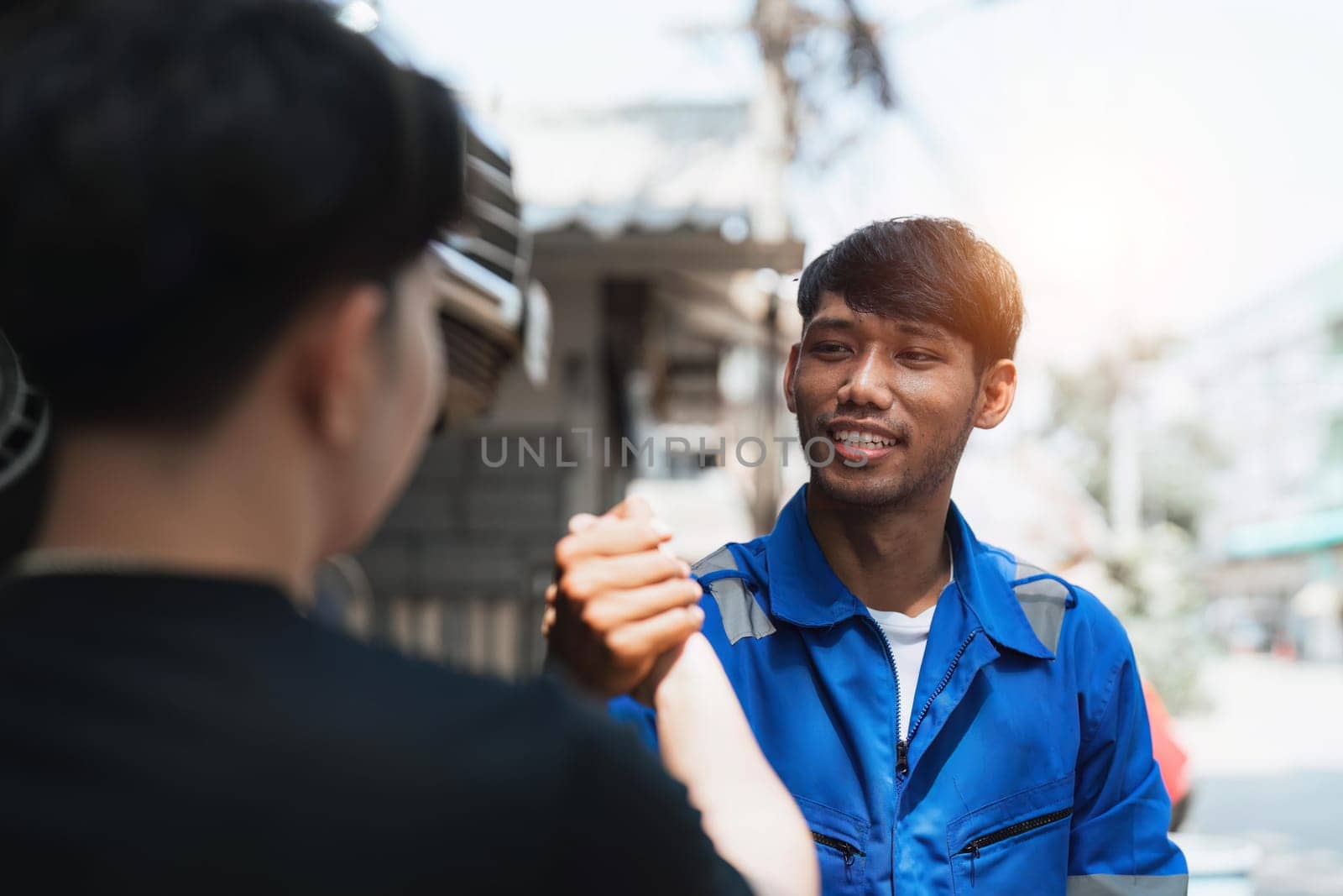 Young man client shaking hands with auto mechanic in red uniform having a deal at the car service.