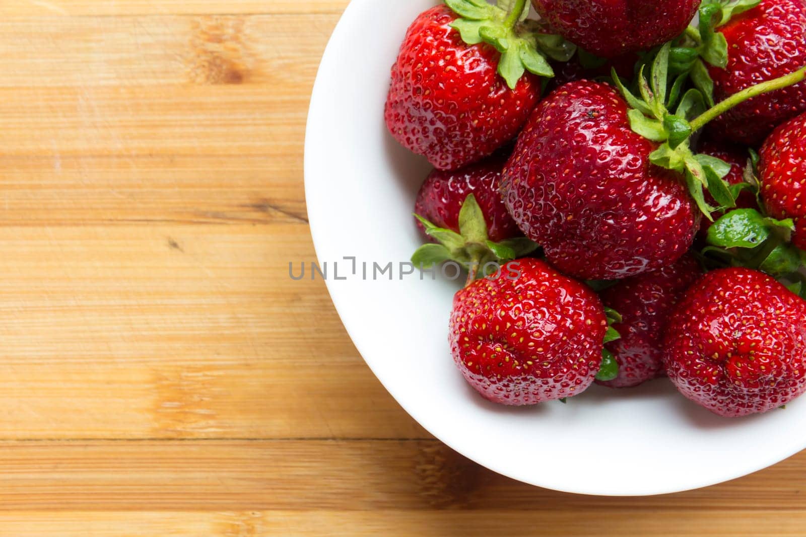 Large, red strawberries lie in a white plate on a wooden surface