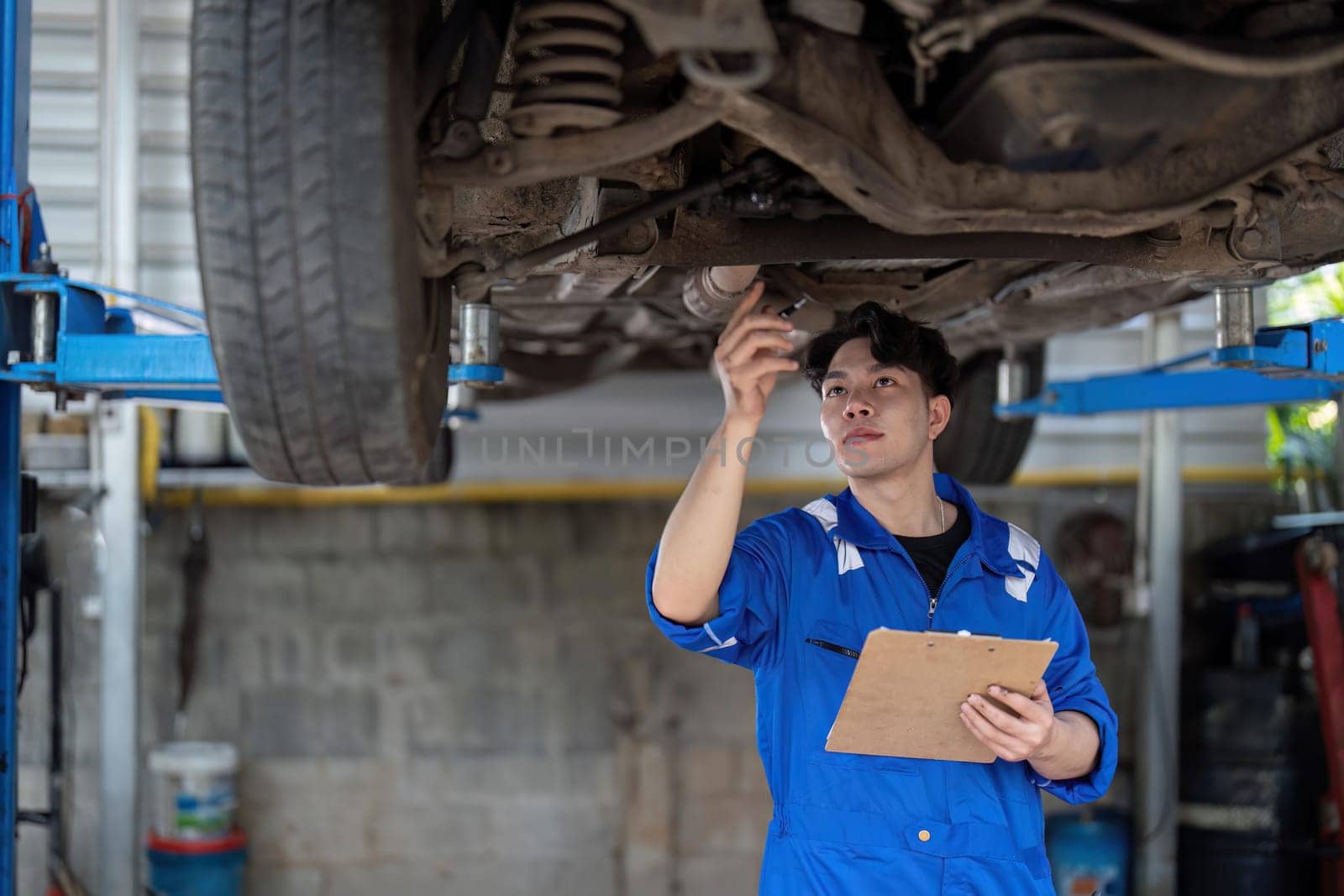 Vehicle service maintenance asian man checking under car condition in garage. Automotive mechanic maintenance checklist document. Car repair service concept.