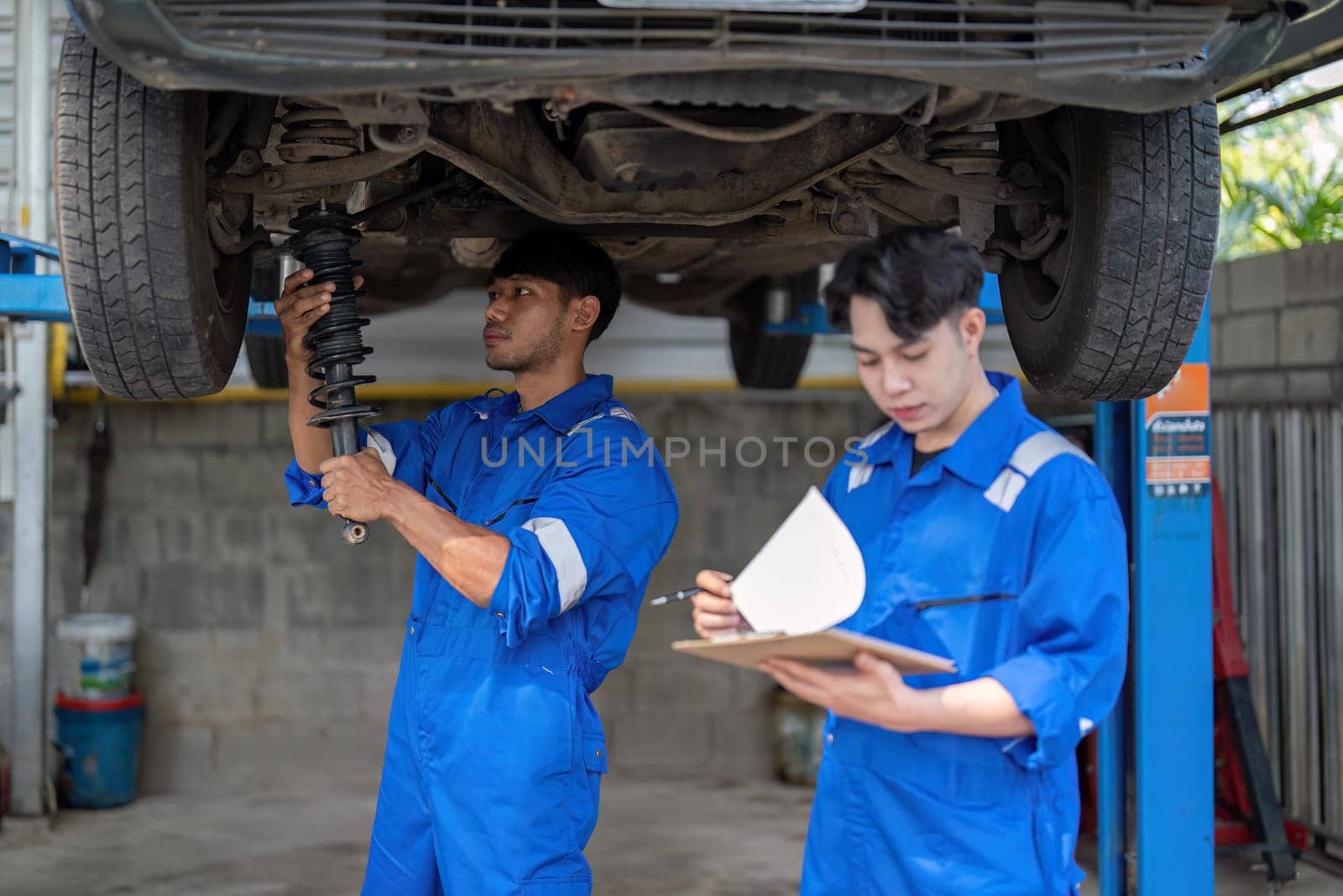 Mechanic man shows report to the asian coworker at garage, A man mechanic and his son discussing repairs done vehicle. Changing automobile business..