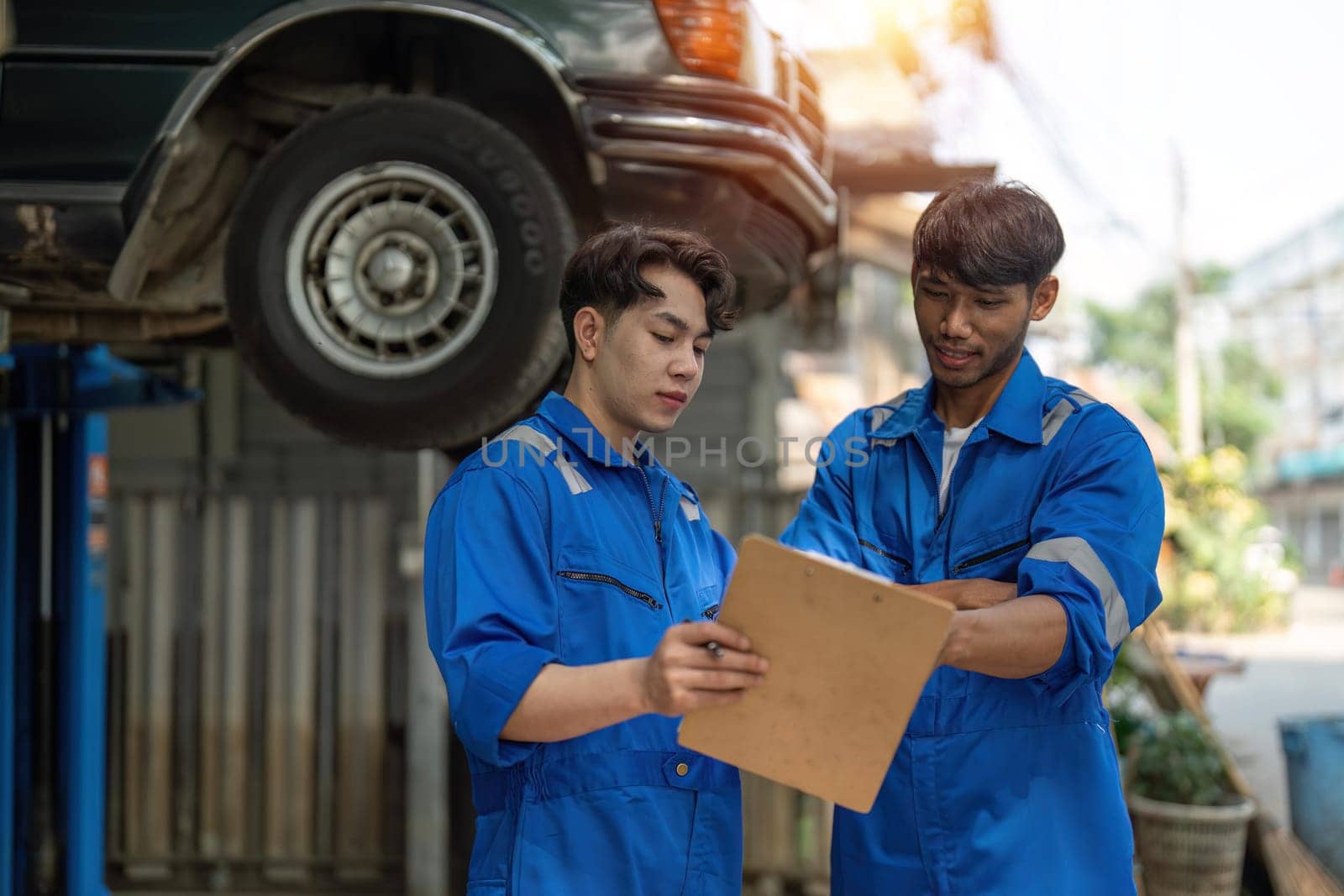 Two Asian automotive mechanic repairman handshake in garage. Vehicle service manager working in mechanics workshop, feel happy and success after check and maintenance car engine for customer. by nateemee