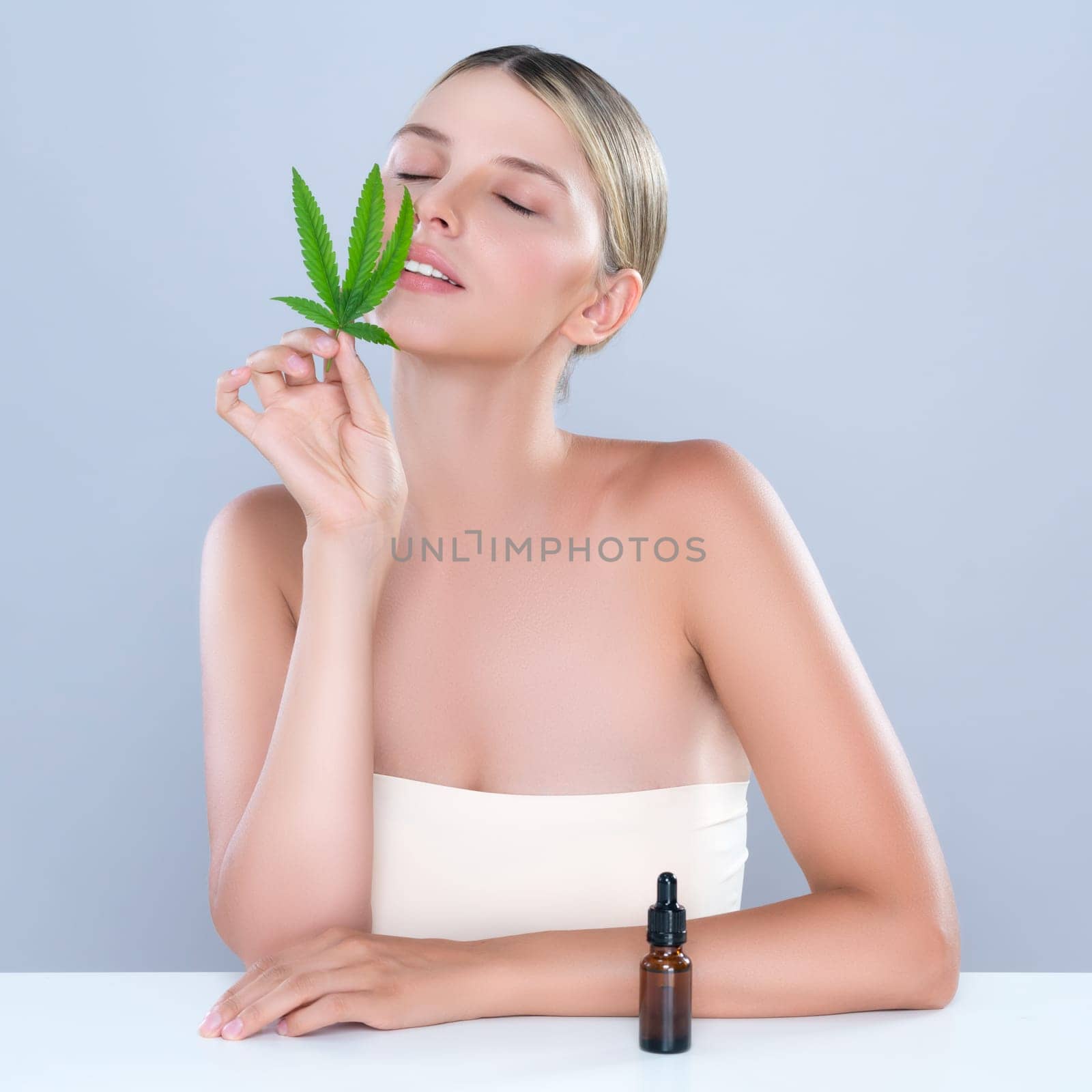 Alluring portrait of beautiful woman holding green leaf with CBD oil bottle. by biancoblue