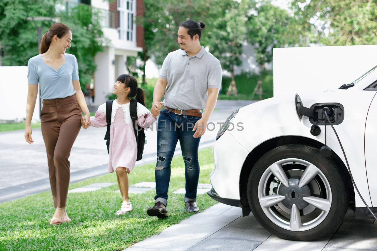 Progressive young happy family with electric vehicle and home backyard charging station. Green and clean energy from electric vehicles for healthy environment. Eco power from renewable source.