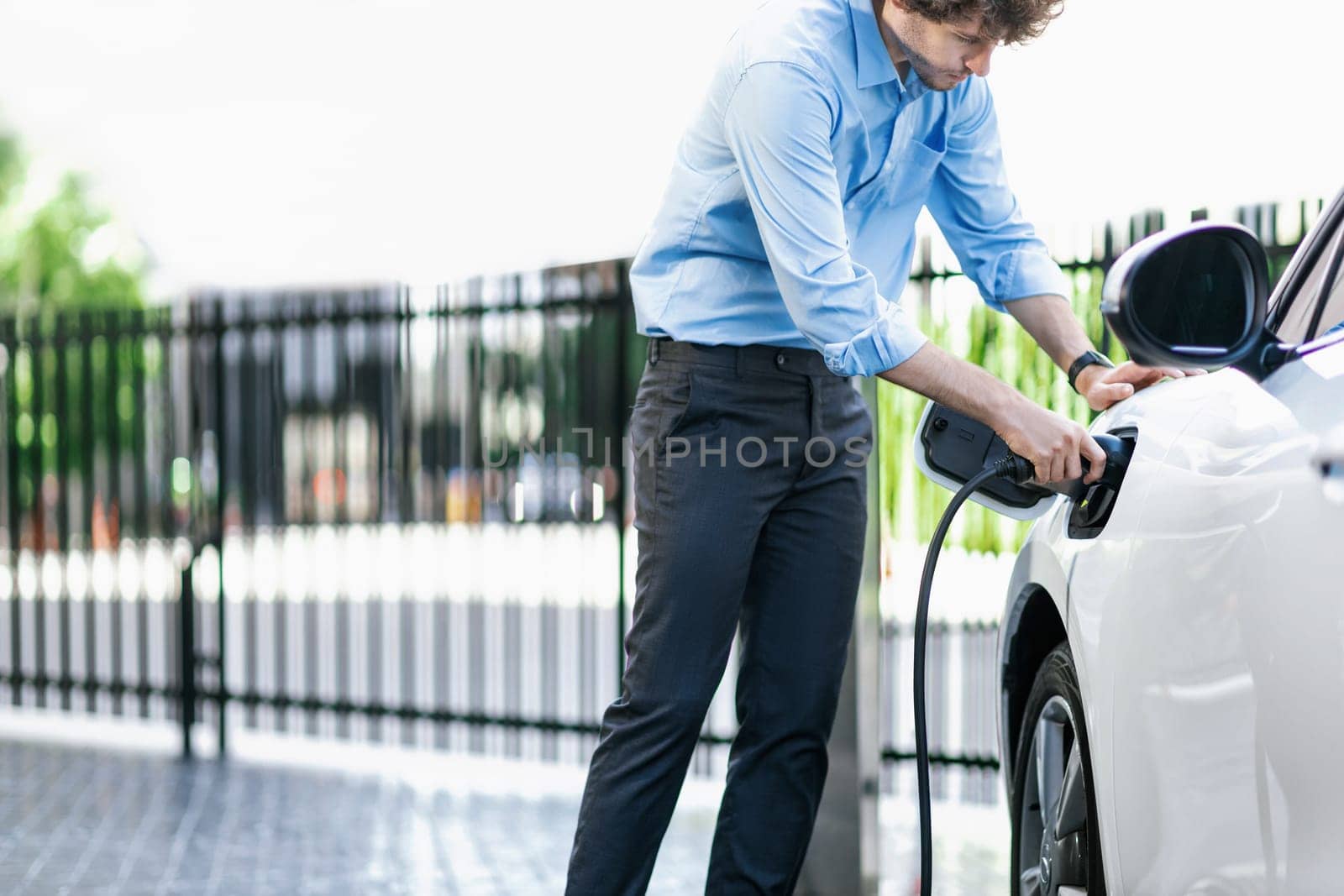 Progressive businessman plugs charger plug from charging station to EV. by biancoblue