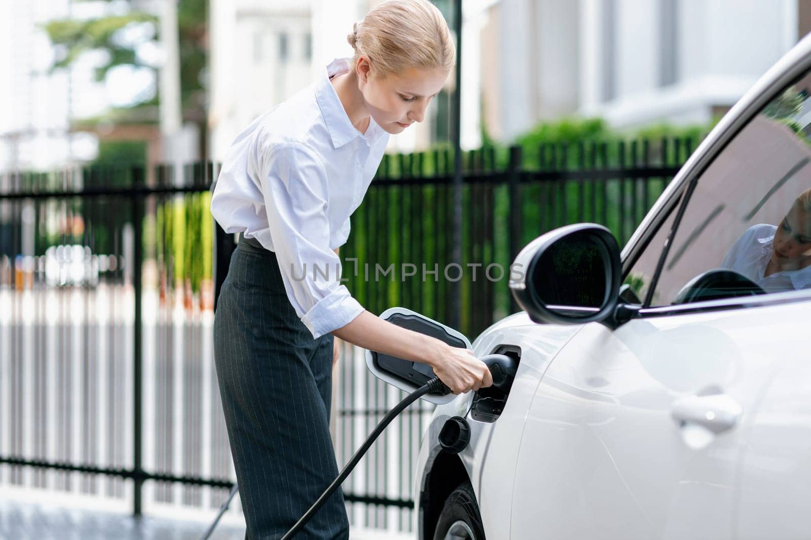Progressive businesswoman plugs charger plug from charging station to EV. by biancoblue