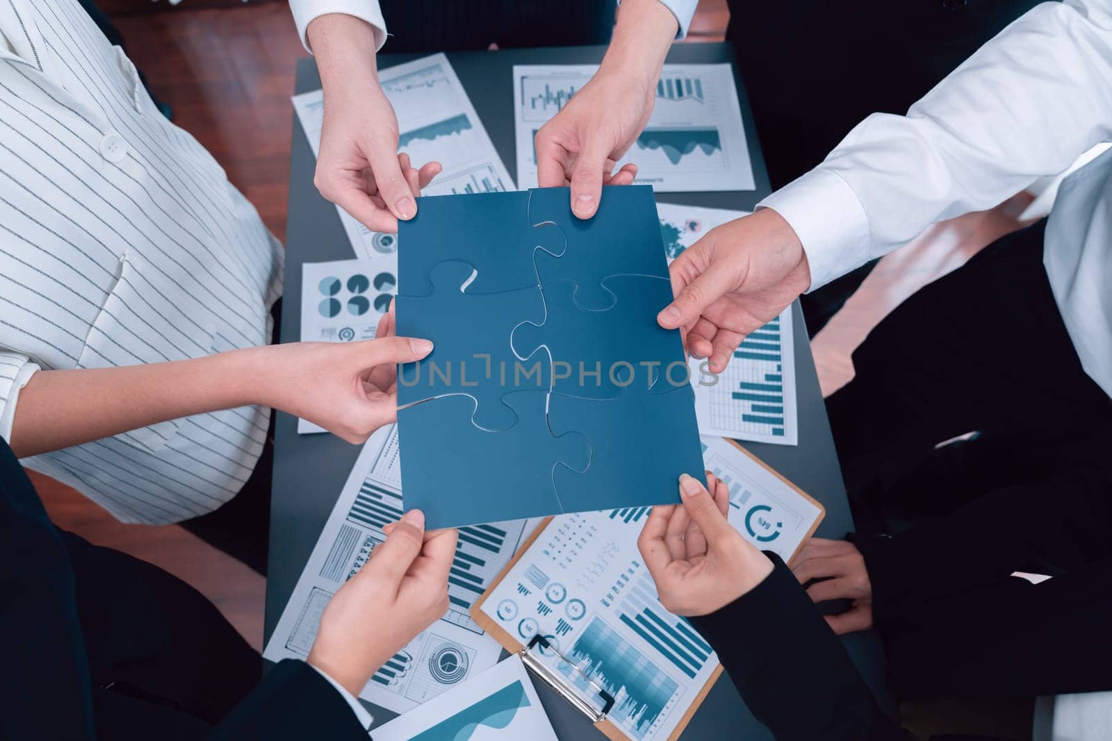 Closeup top view business team of office worker putting jigsaw puzzle together over table filled with financial report paper in workplace with manager to promote harmony concept in meeting room.