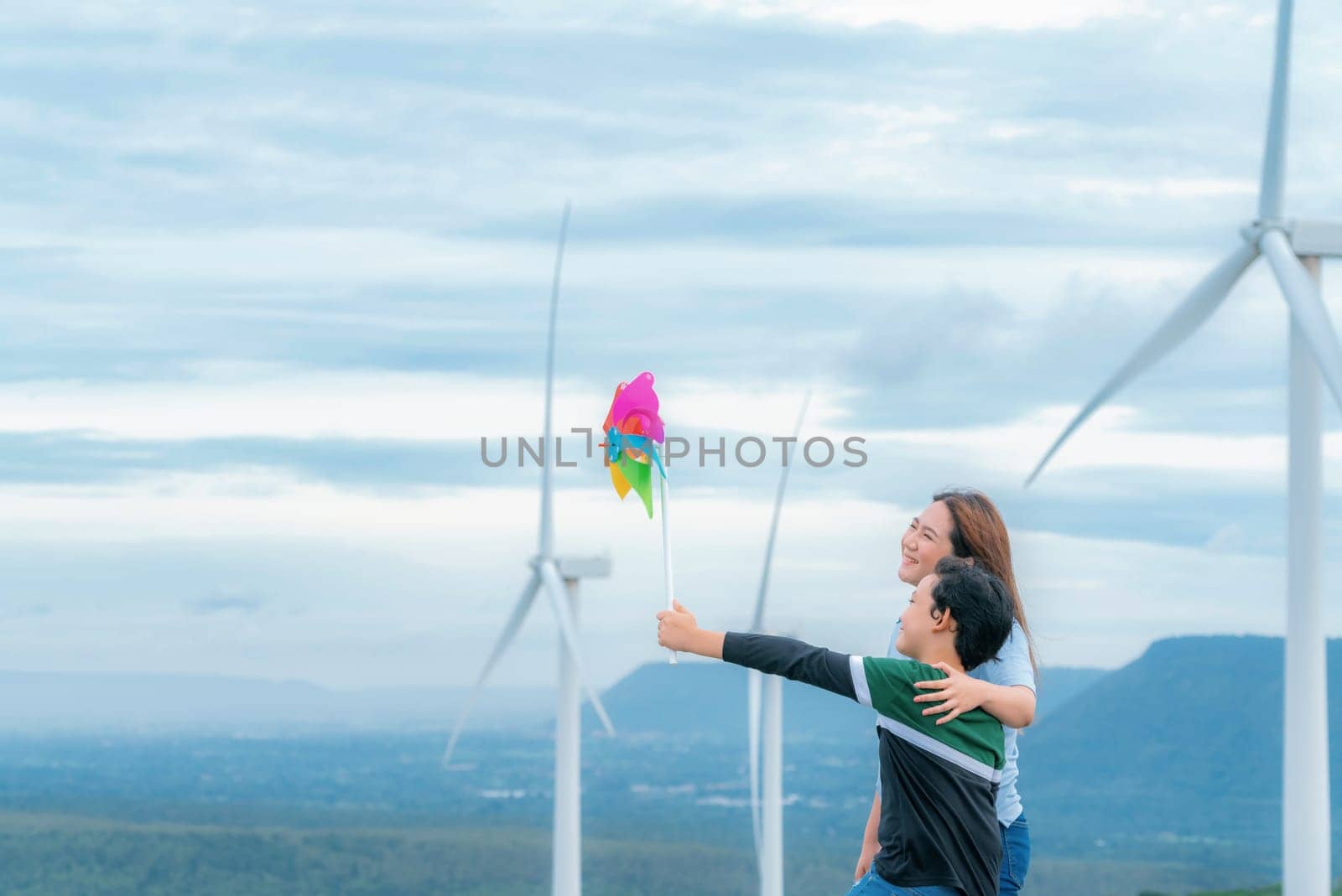 A progressive mother and her son are on vacation, enjoying the natural beauty of a lake at the bottom of a hill while the boy carries a toy windmill.