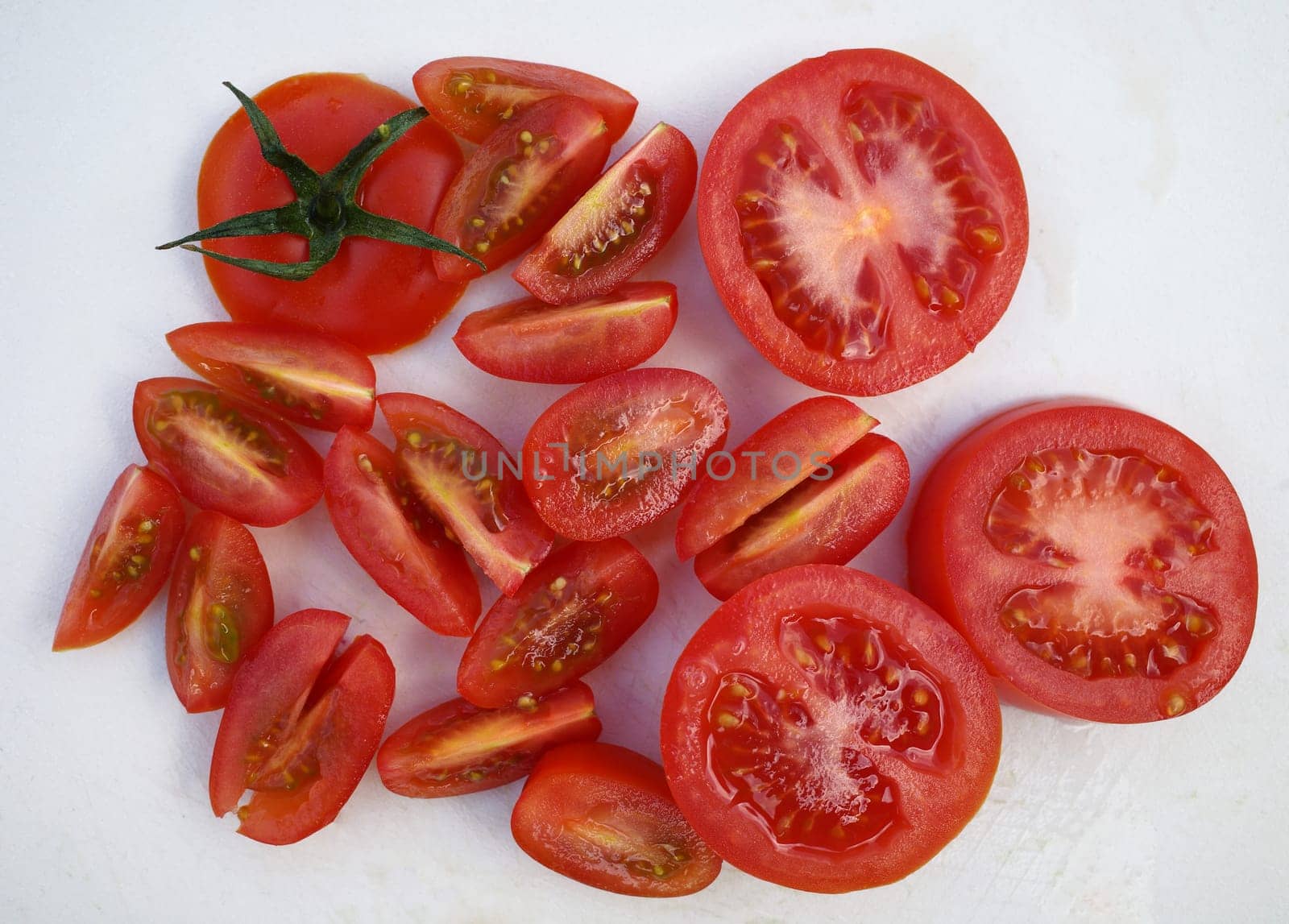 Sliced ​​red tomato combined with quartered cherry tomatoes on a white cutting board