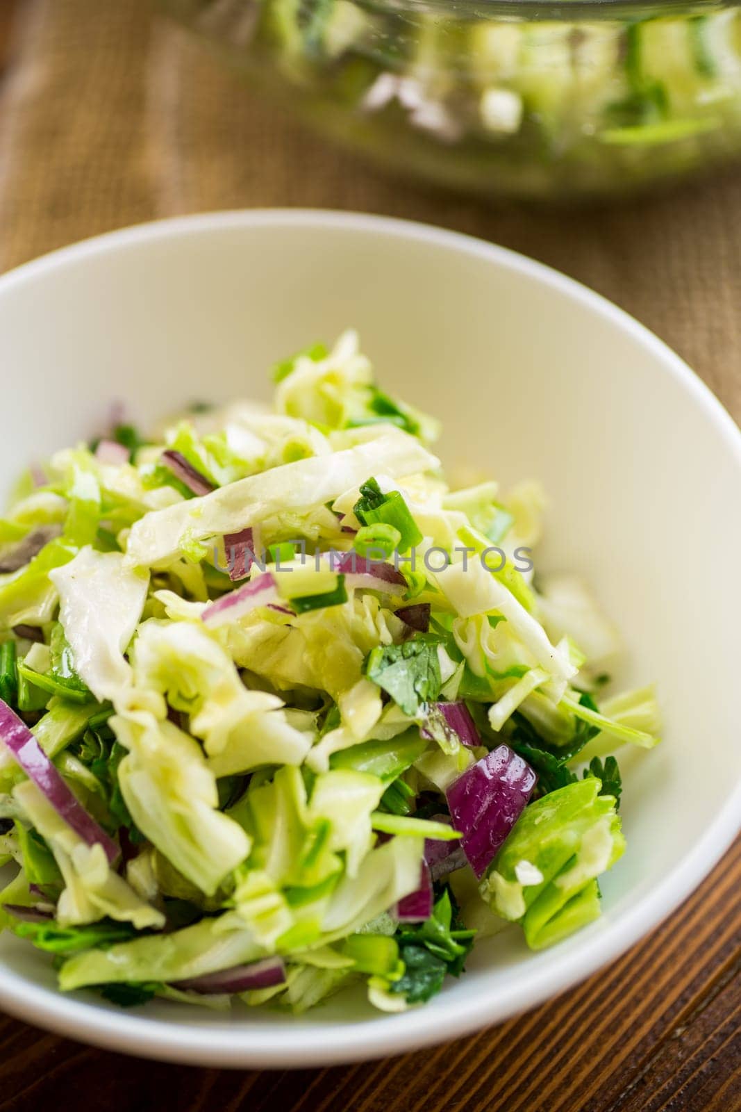 Young cabbage salad with purple onions in a bowl on a wooden table.