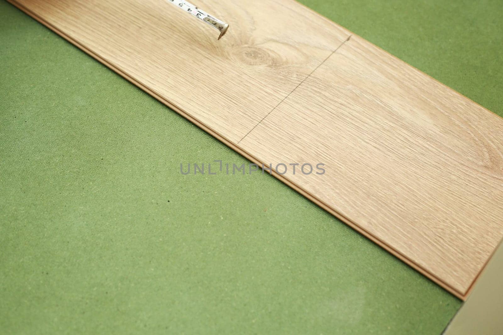 Installation laminate or parquet in the room, worker installing wooden laminate flooring, marking the length of the laminate. laying laminate flooring at home. measuring with a tape measure.