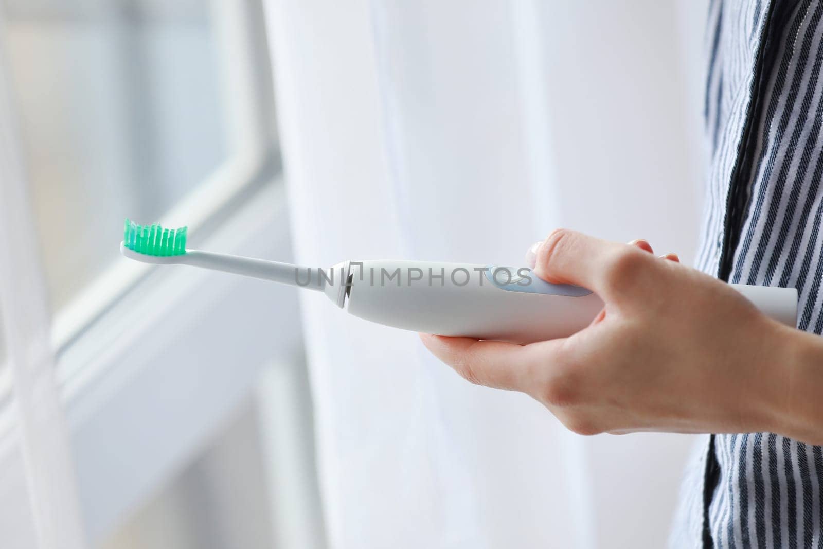 woman using electric toothbrush at home. technology and health care. by Andriimedvediuk