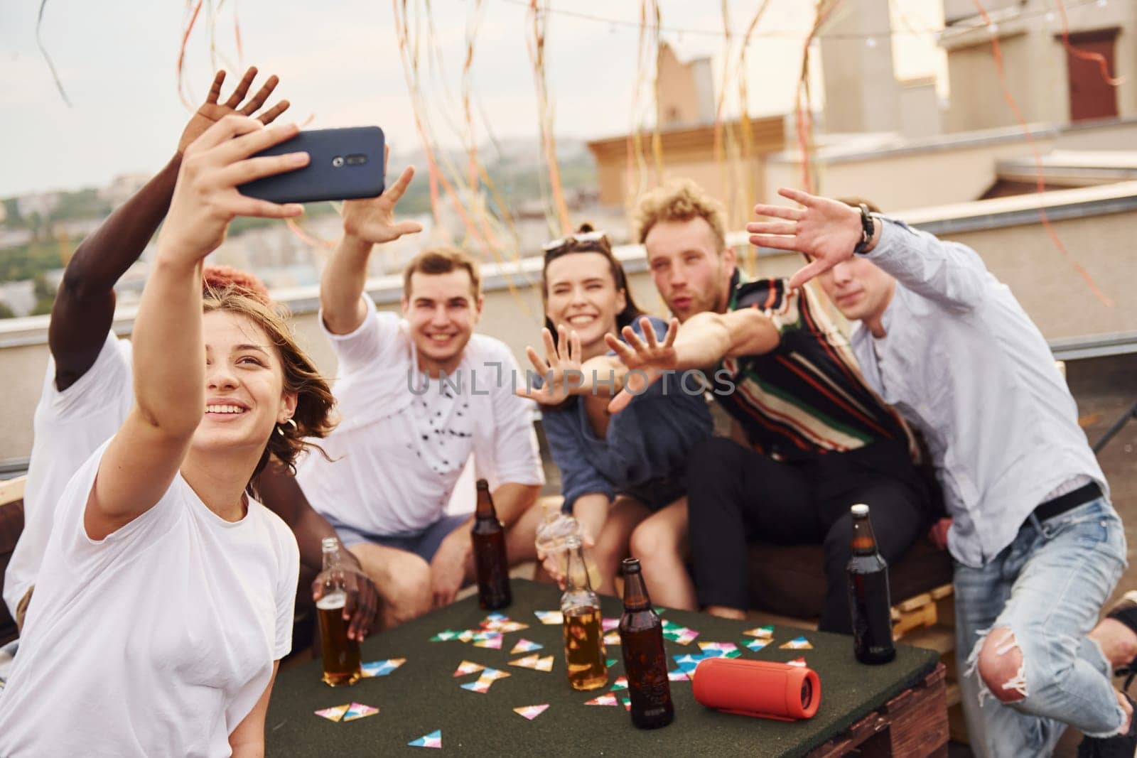 Girl doing photo when people playing card game. Group of young people in casual clothes have a party at rooftop together at daytime.