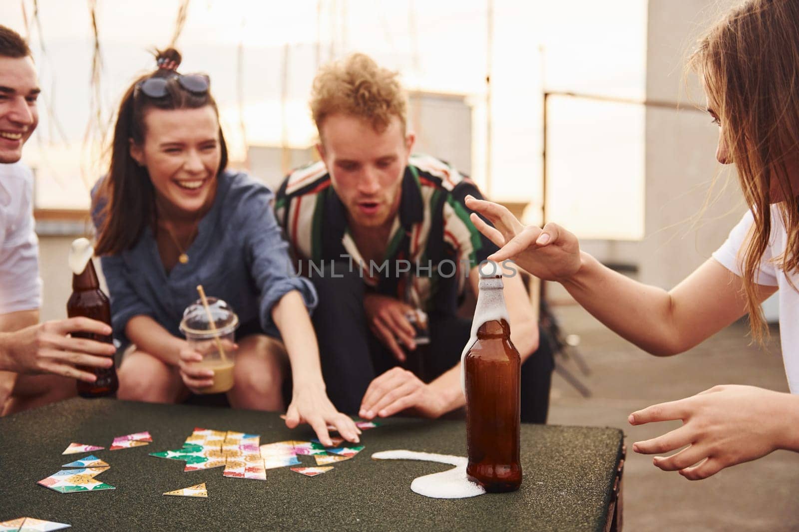 Playing card game. Group of young people in casual clothes have a party at rooftop together at daytime.