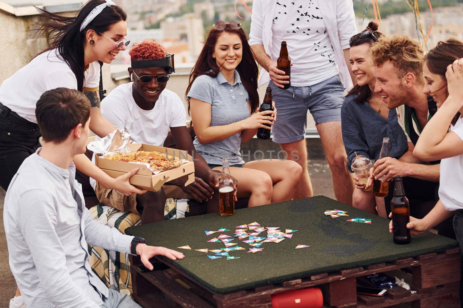 With delicious pizza. Group of young people in casual clothes have a party at rooftop together at daytime.