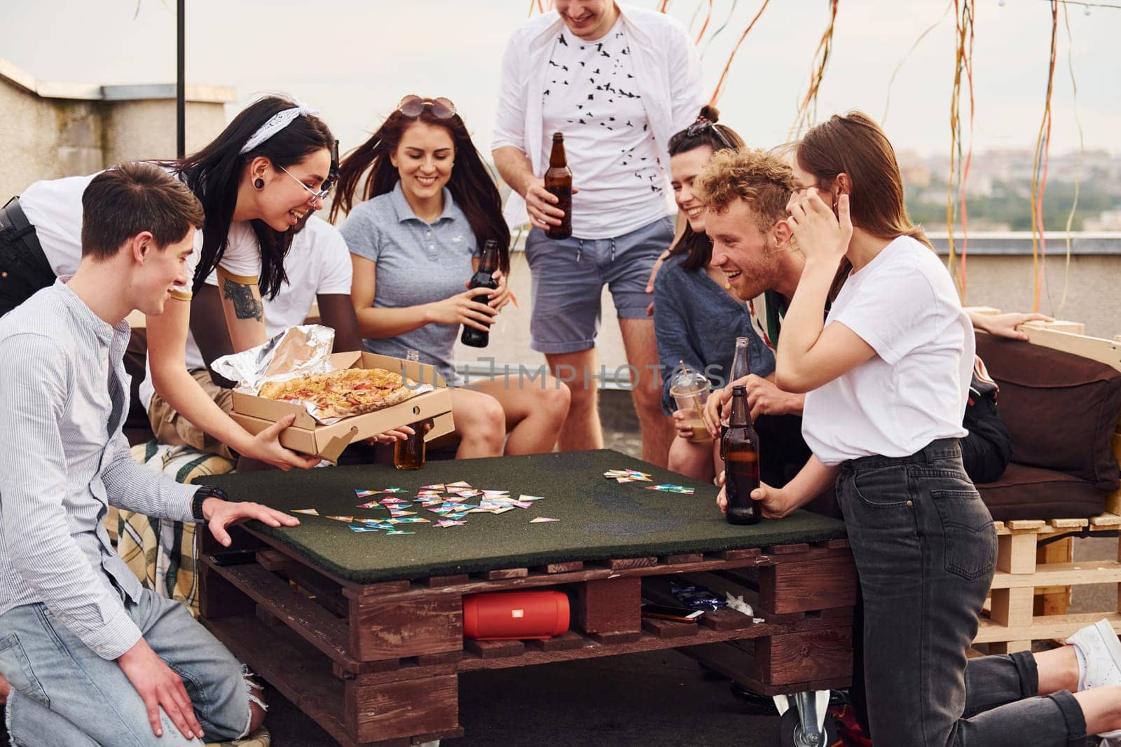 With delicious pizza. Group of young people in casual clothes have a party at rooftop together at daytime.