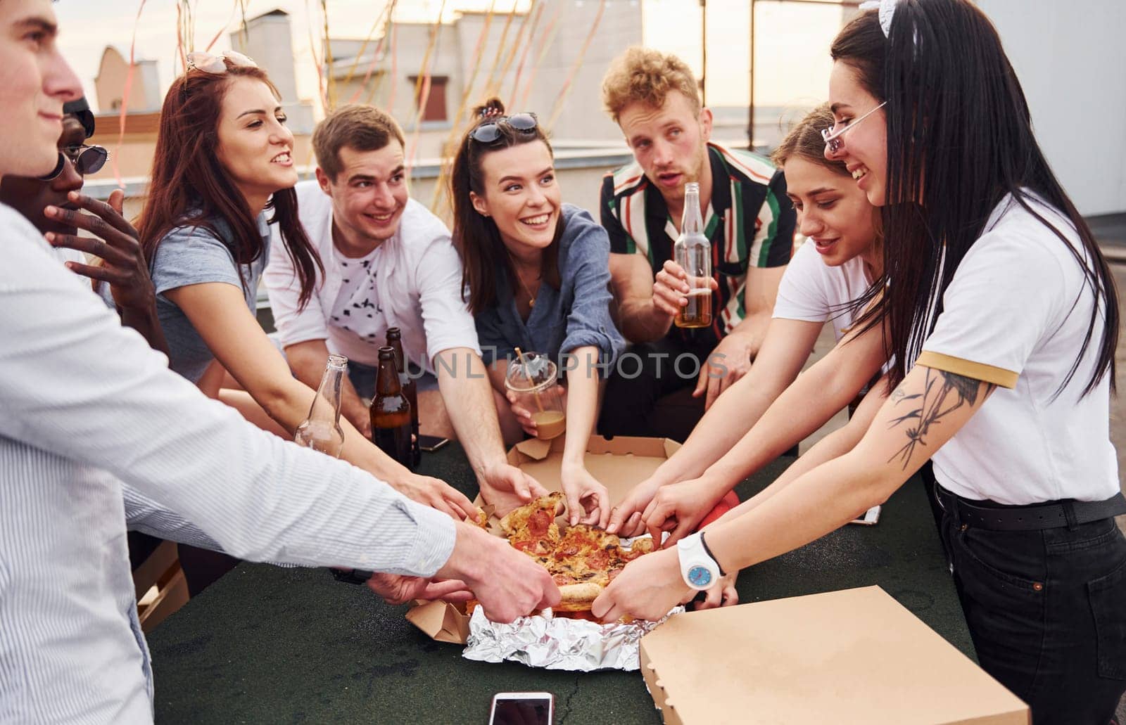 With delicious pizza. Group of young people in casual clothes have a party at rooftop together at daytime.