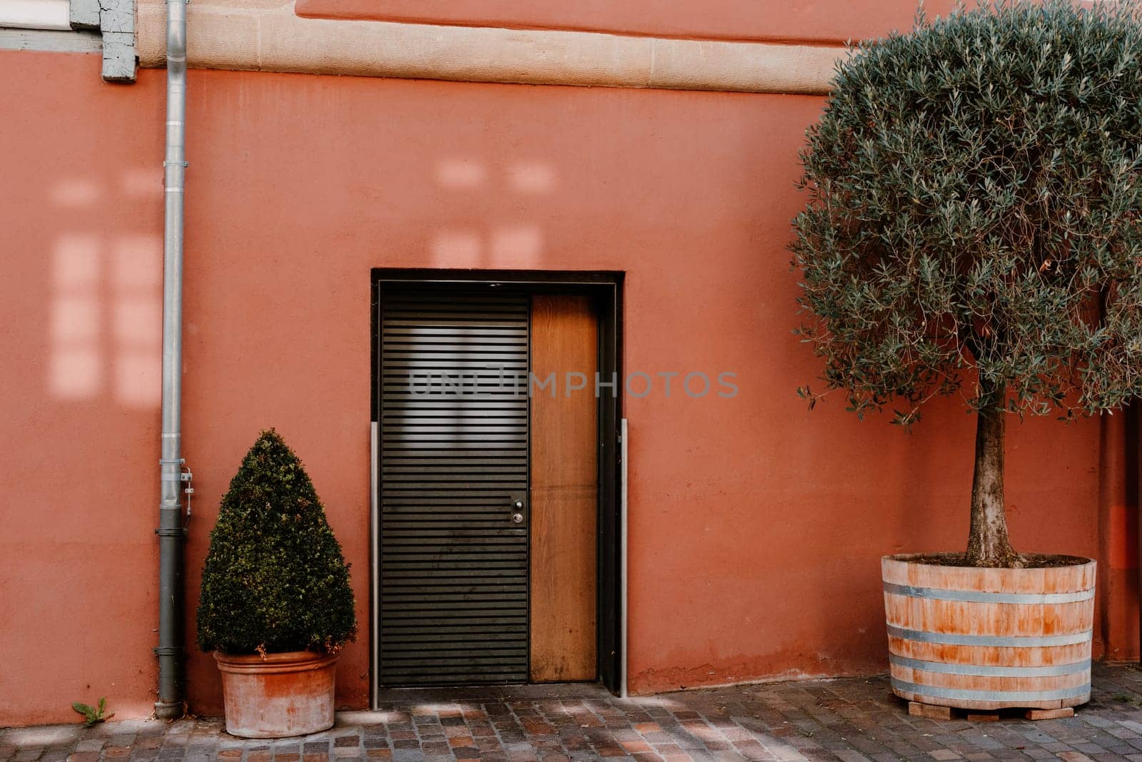 Facade of a modern house with a gray front door and potted flowers. Old historic Italian architecture. Traditional European old town building. Blue wooden door, balcony, blooming bush, pastel walls with sunlight shadows. Aesthetic summer vacation travel background
