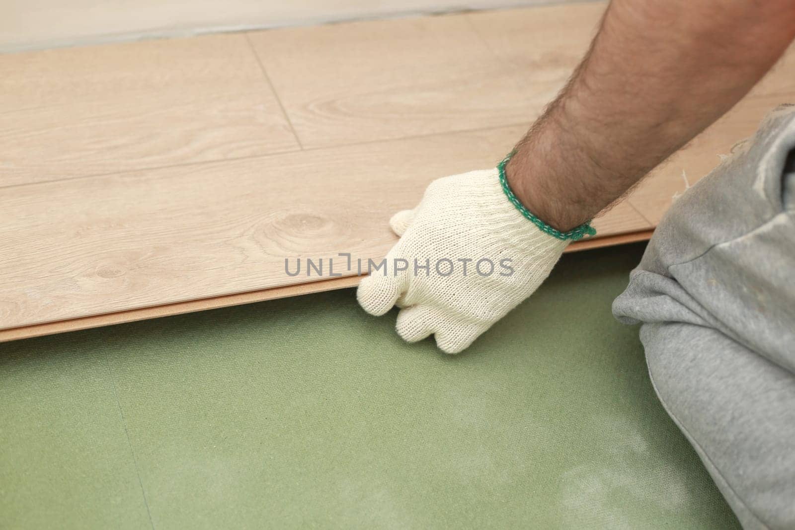 Installing laminate or parquet floor in room, detail on man hands fitting wooden tile, over green foam base.