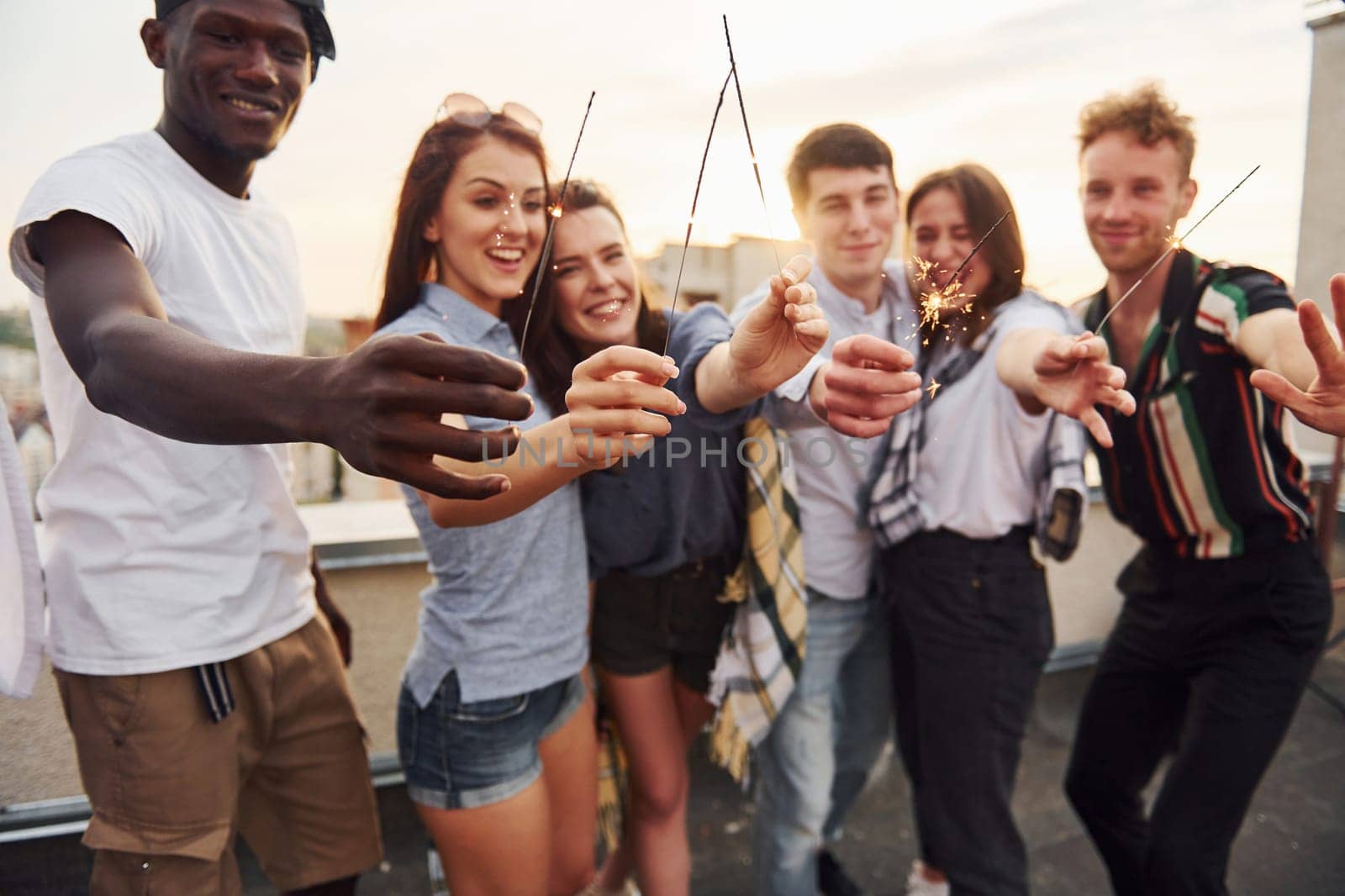 With sparklers in hands. Group of young people in casual clothes have a party at rooftop together at daytime.