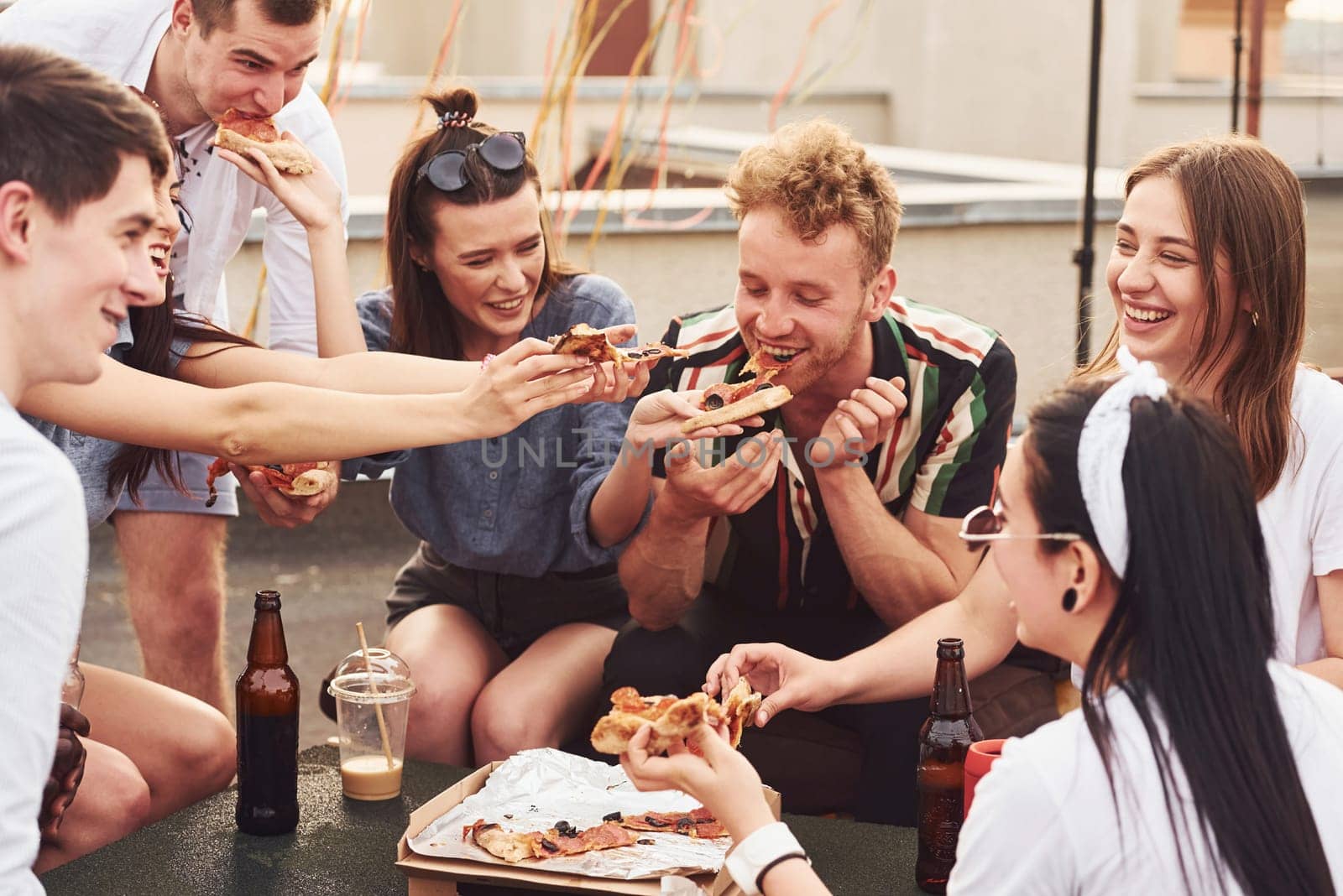 Delicious pizza. Group of young people in casual clothes have a party at rooftop together at daytime.