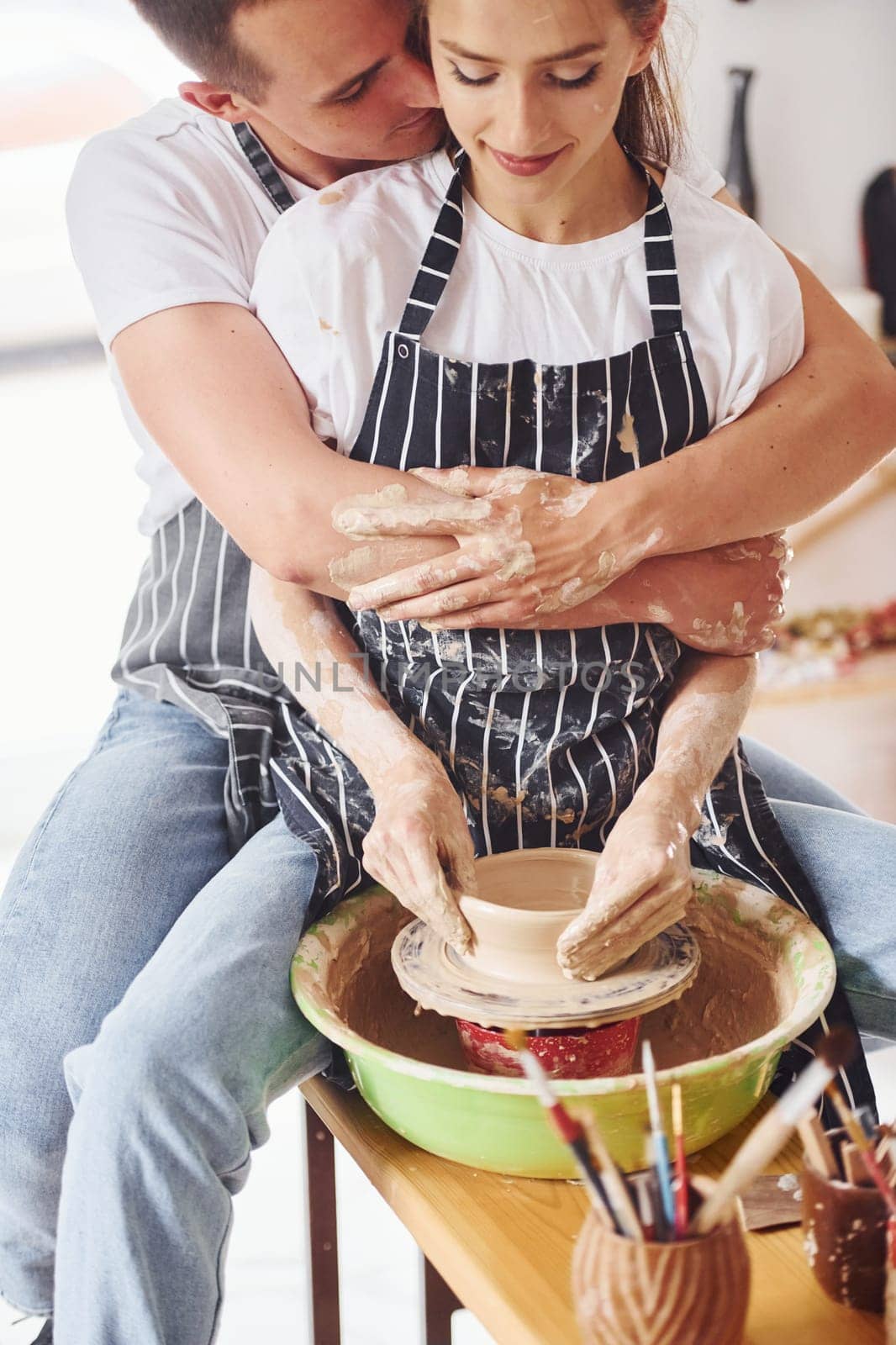 With her boyfriend or husband. Young female ceramist indoors with handmade clay product. Conception of pottery.