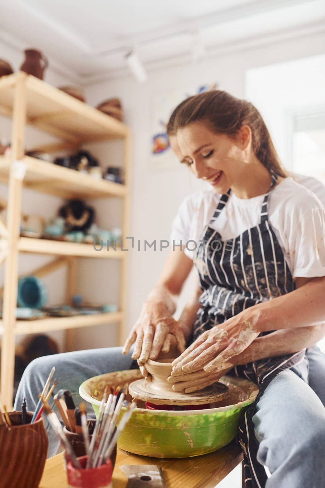 With her boyfriend or husband. Young female ceramist indoors with handmade clay product. Conception of pottery.