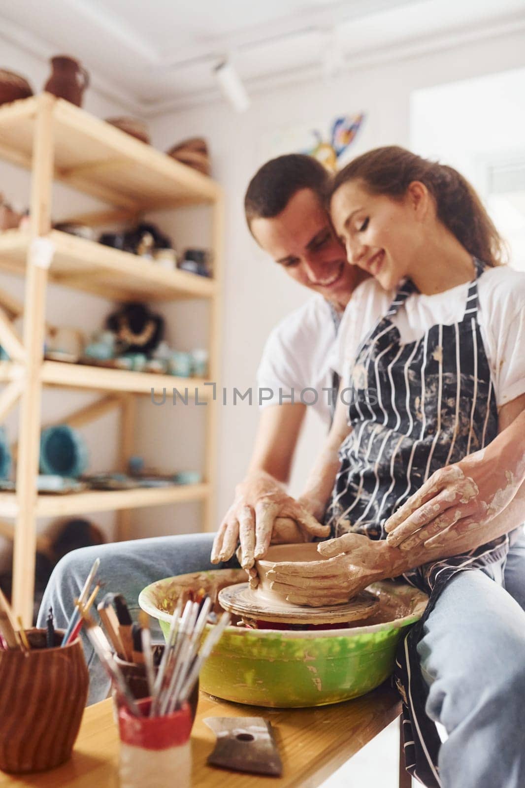 With her boyfriend or husband. Young female ceramist indoors with handmade clay product. Conception of pottery.