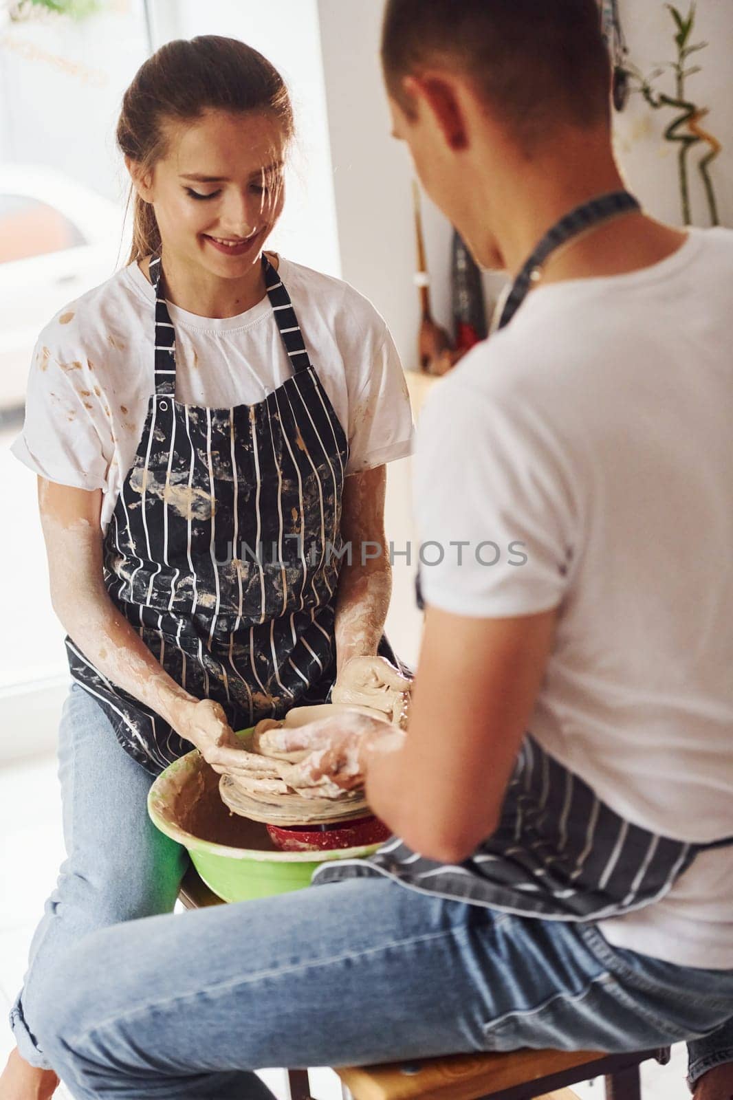 With her boyfriend or husband. Young female ceramist indoors with handmade clay product. Conception of pottery.