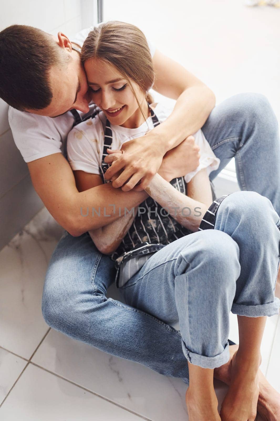 Cute young couple in jeans sitting down on the floor and embracing each other.