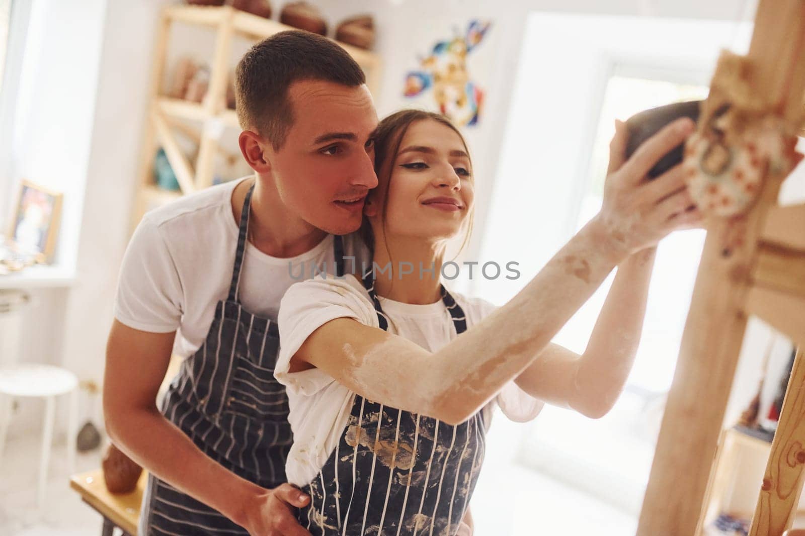 Job is done. With her boyfriend or husband. Young female ceramist indoors with finished handmade clay product. Conception of pottery.