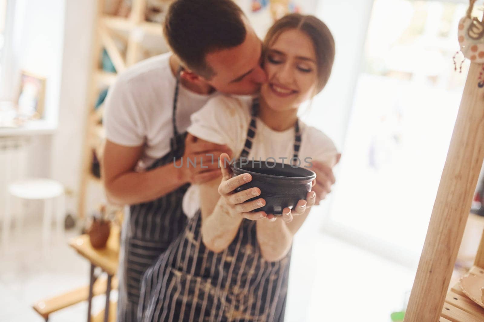 Job is done. With her boyfriend or husband. Young female ceramist indoors with finished handmade clay product. Conception of pottery.