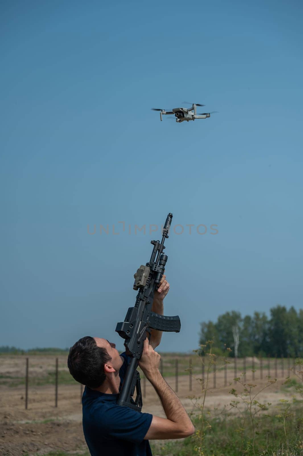 A man aims to shoot a rifle at a flying drone against a blue sky. by mrwed54