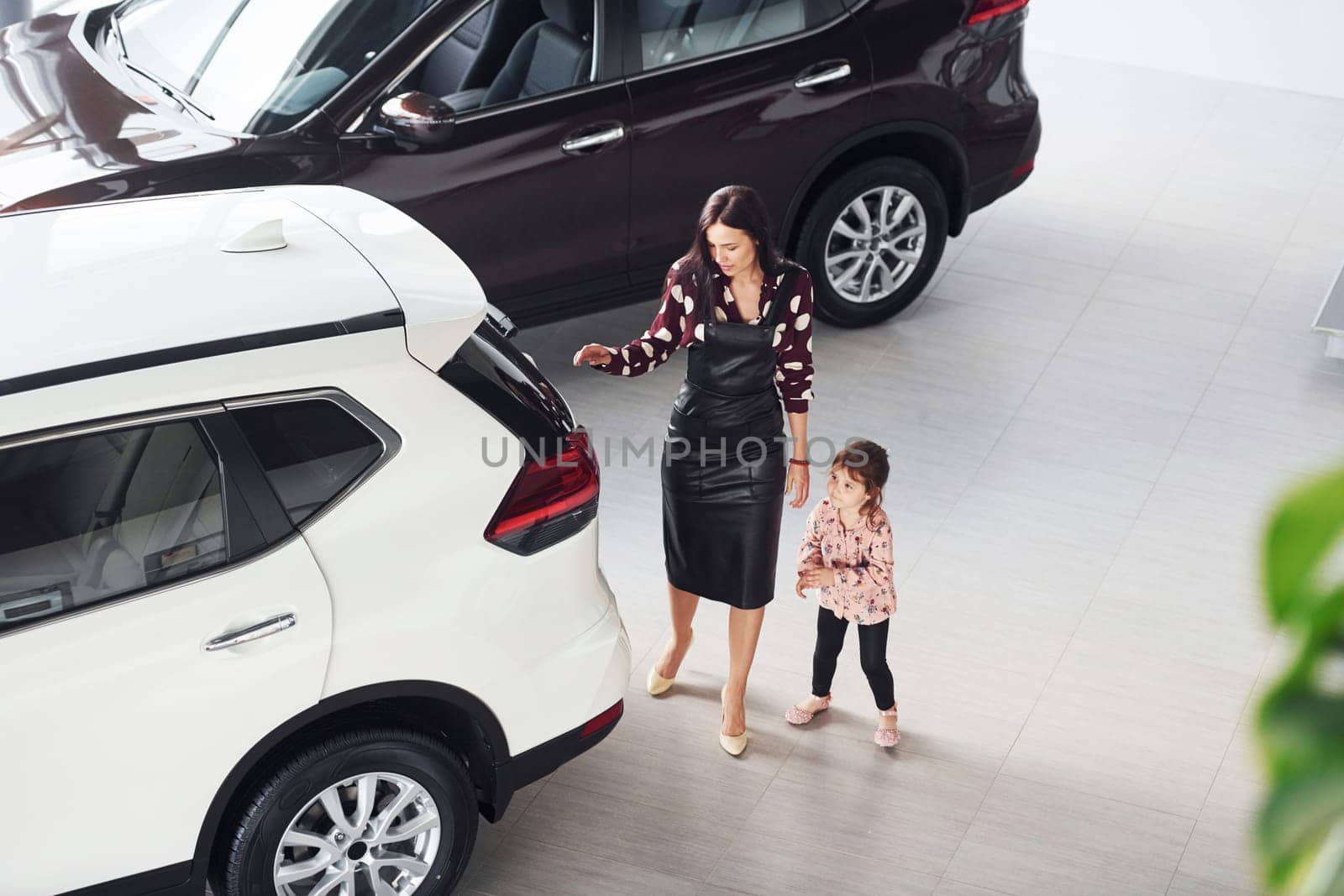Mother with her daughter walking together near modern automobile indoors.