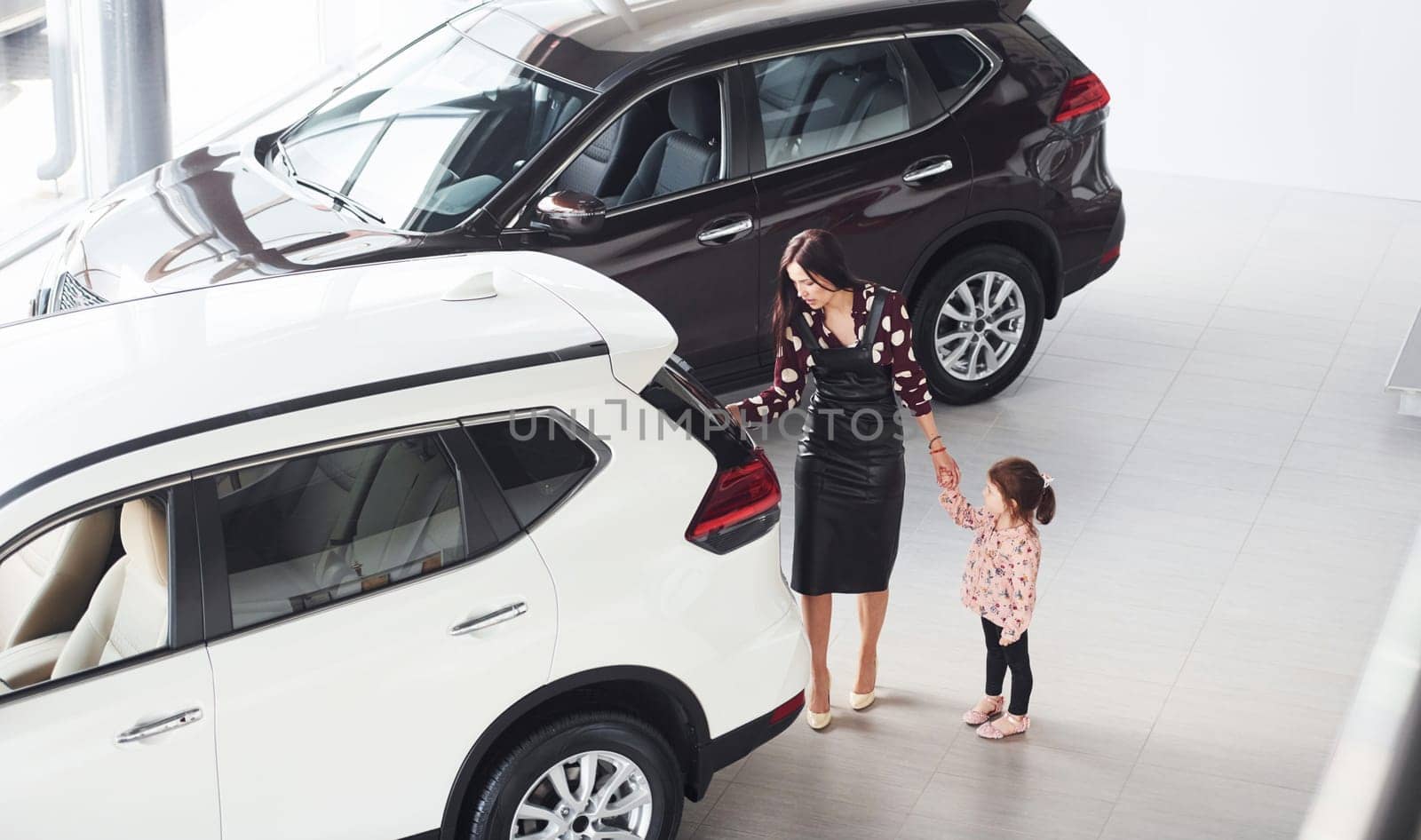 Mother with her daughter walking together near modern automobile indoors.