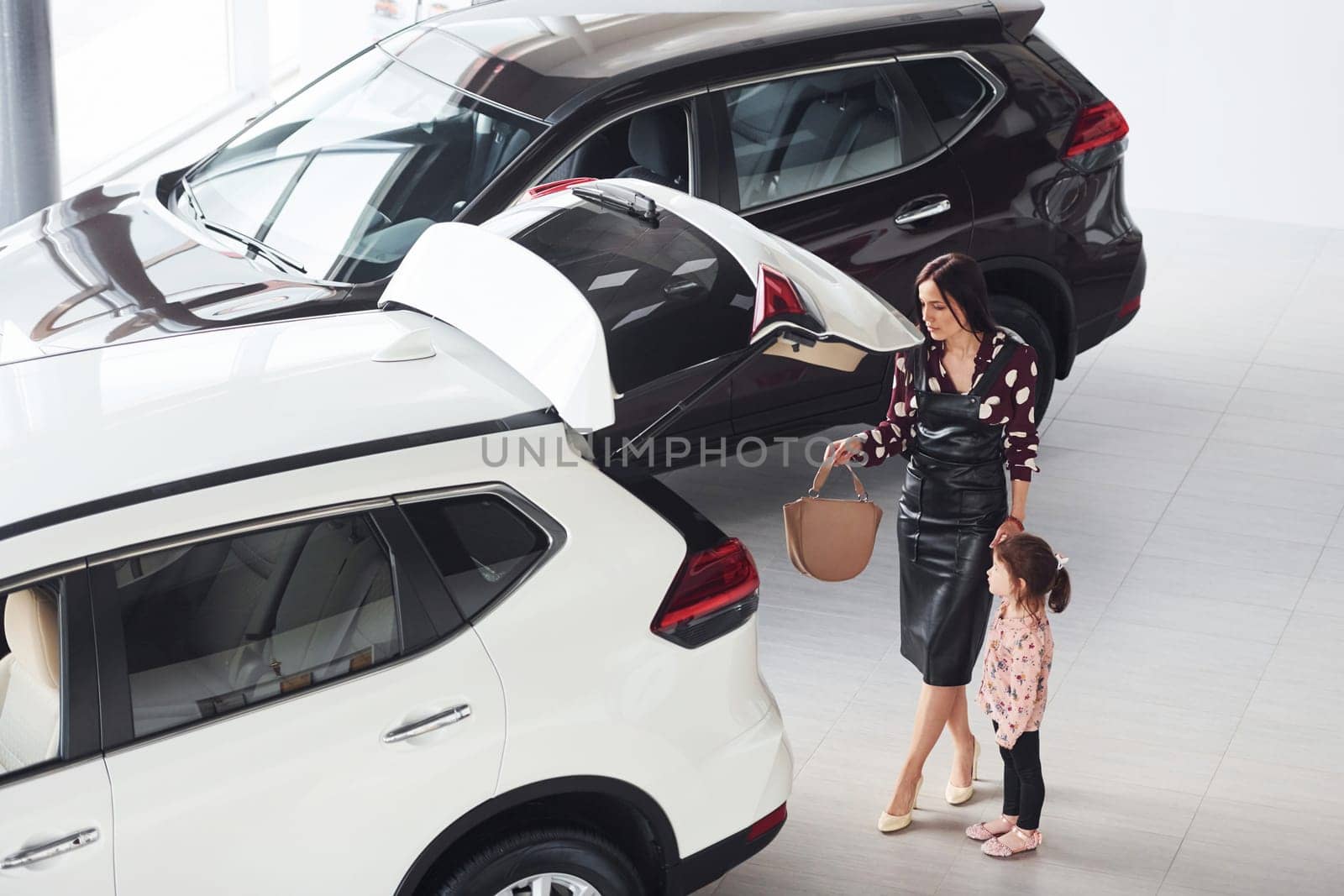 Mother with her daughter walking together near modern automobile indoors.