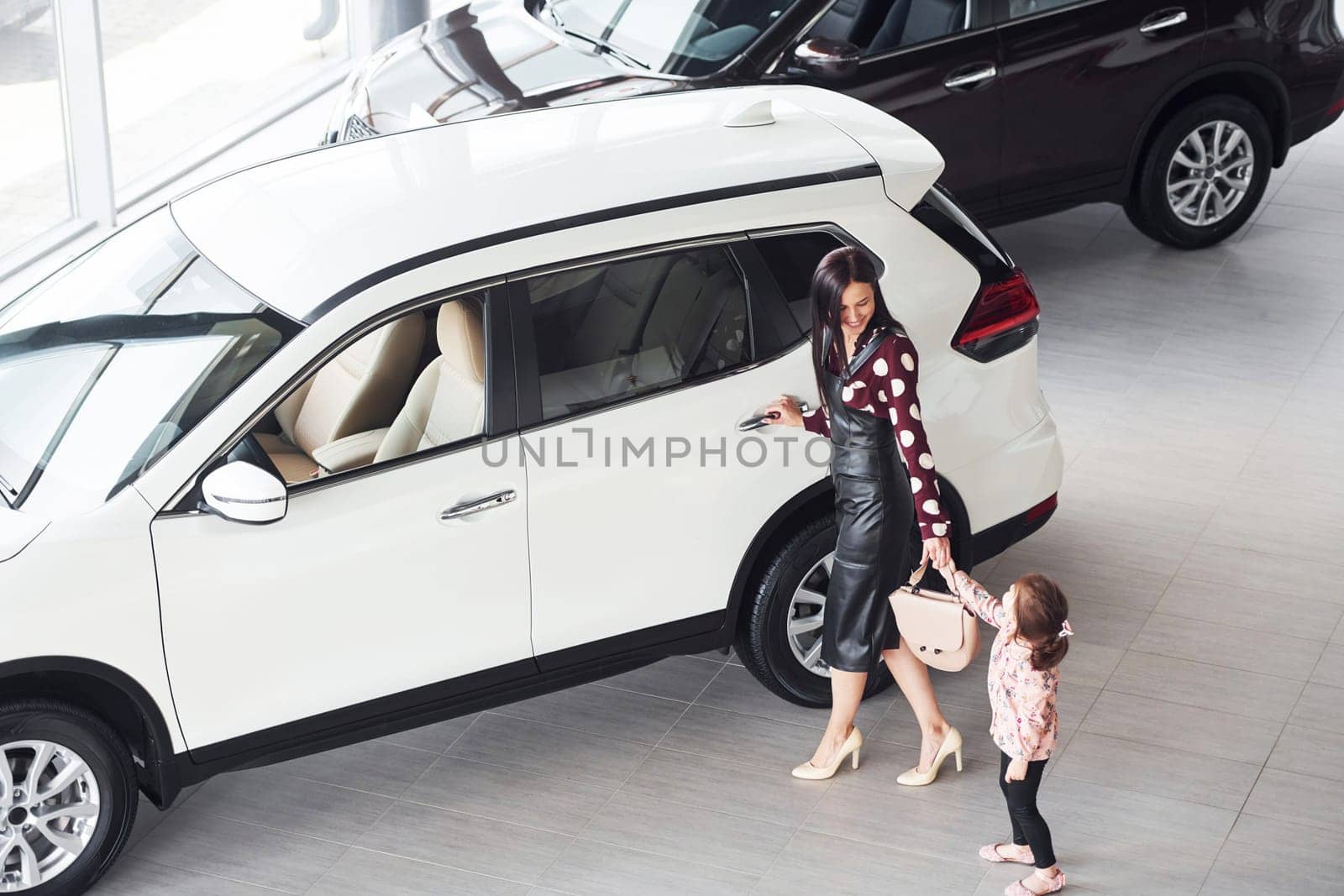 Mother with her daughter walking together near modern automobile indoors.