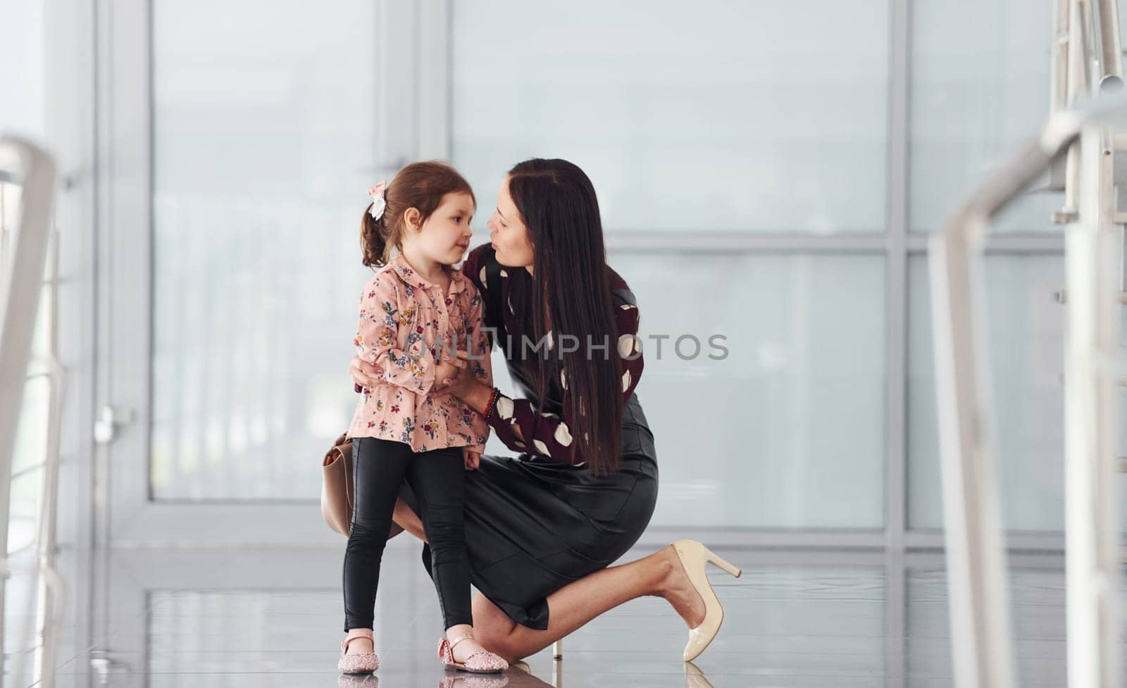 Young mother with her daughter walking together indoors in the office or airport. Having vacation.