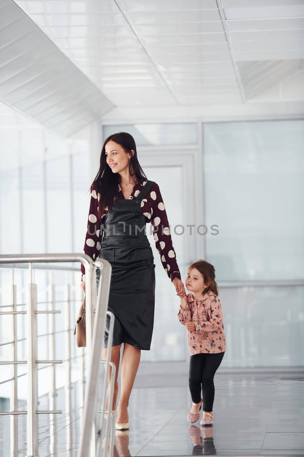 Young mother with her daughter walking together indoors in the office or airport. Having vacation.